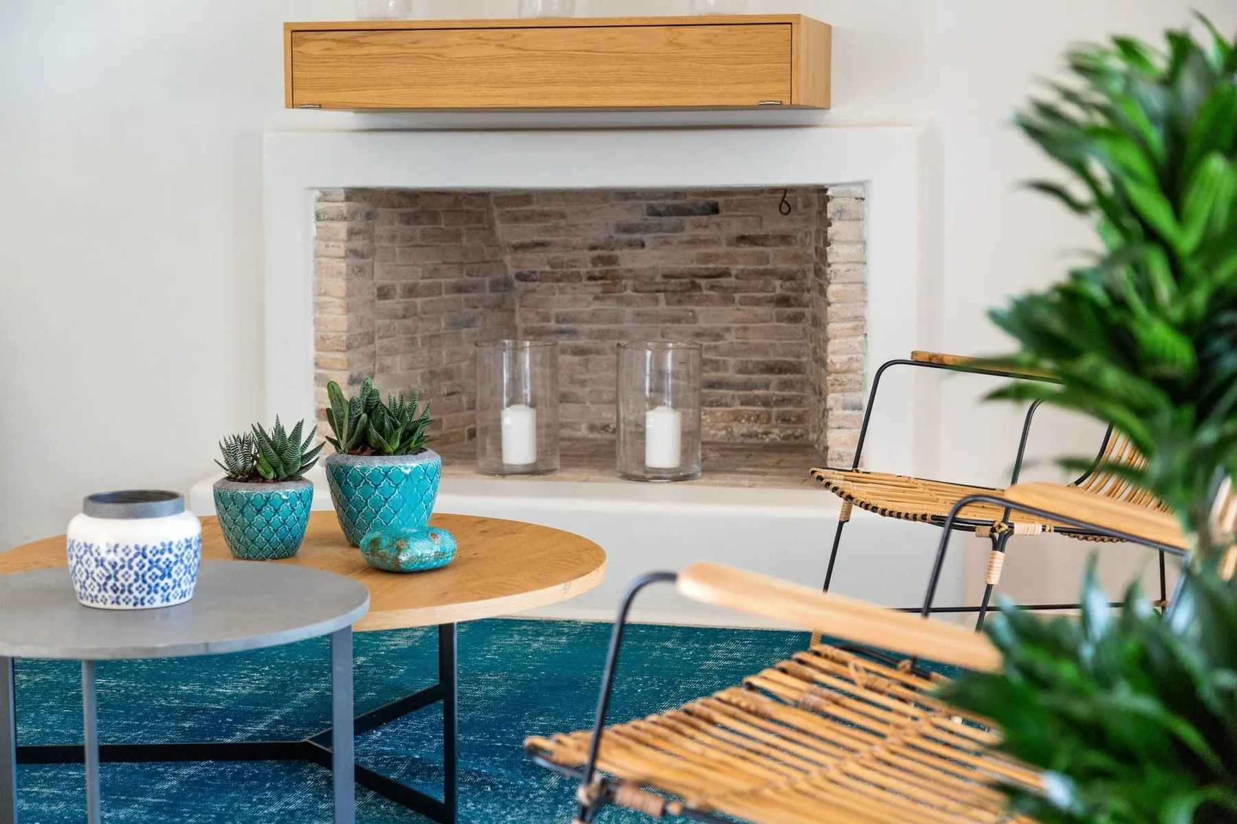 A living room seating area with a round coffee table, woven chairs, and potted plants.