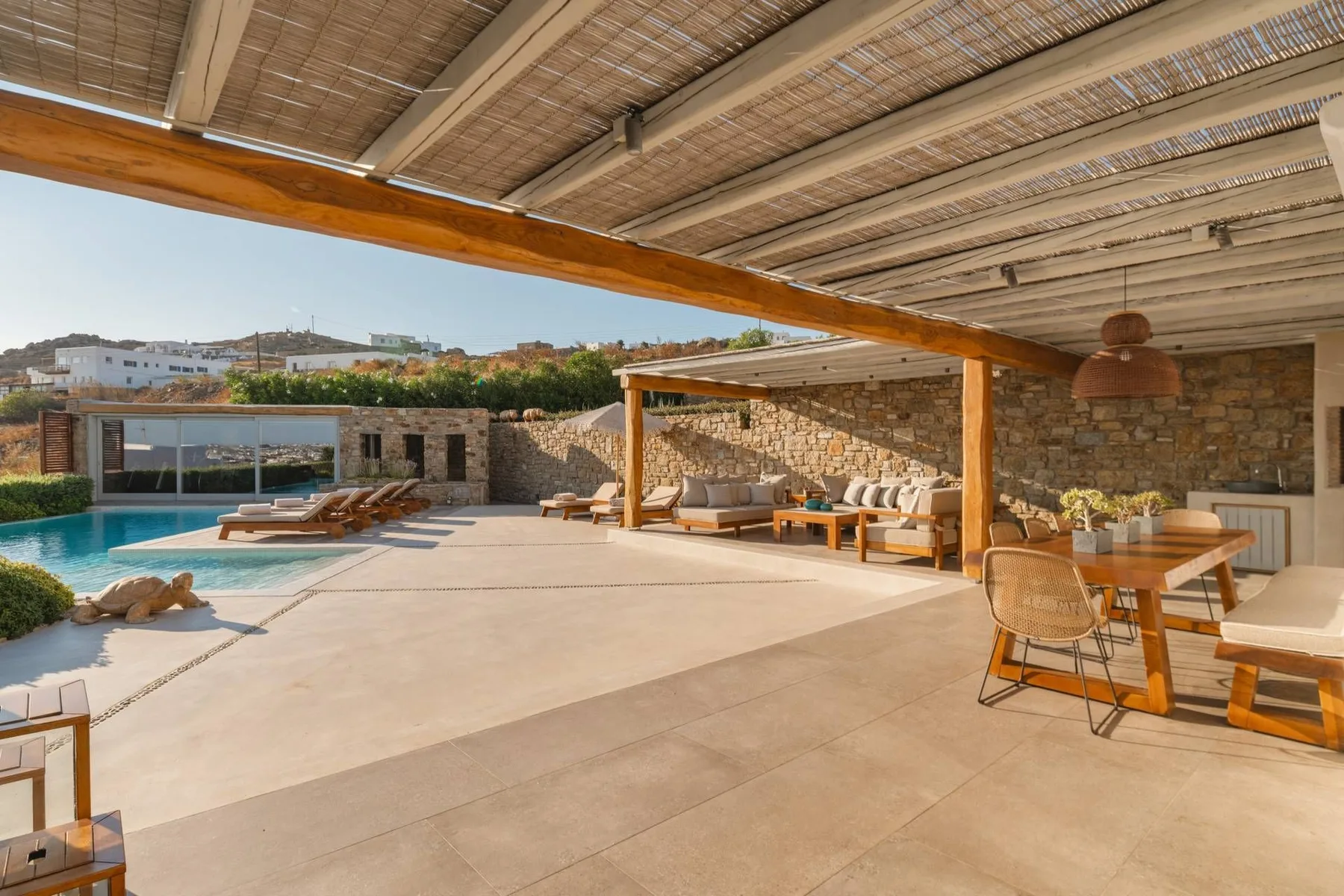 A covered outdoor patio with seating overlooks a swimming pool.