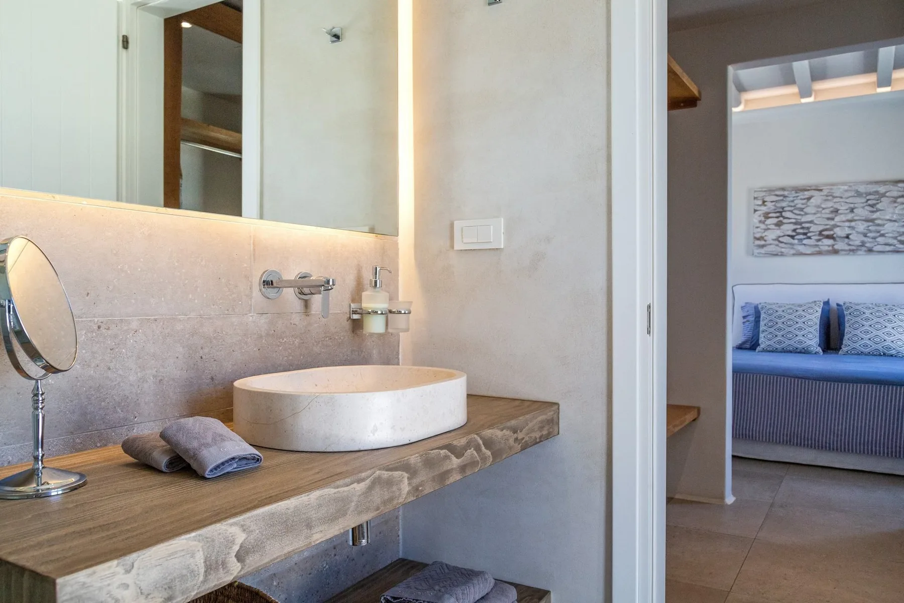 A bathroom vanity with a vessel sink and mirror opens onto a bedroom.