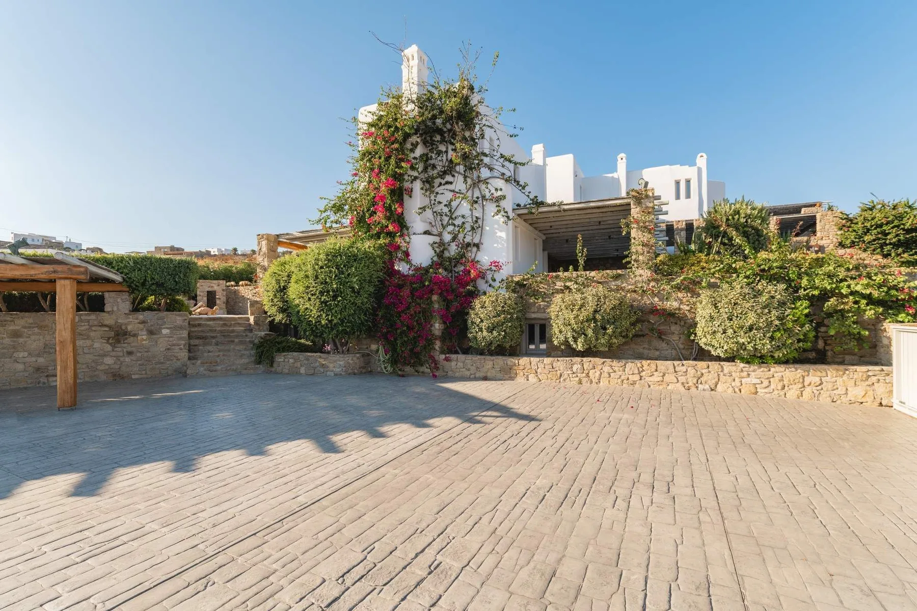 A paved courtyard bordered by low stone walls, greenery, and white buildings.