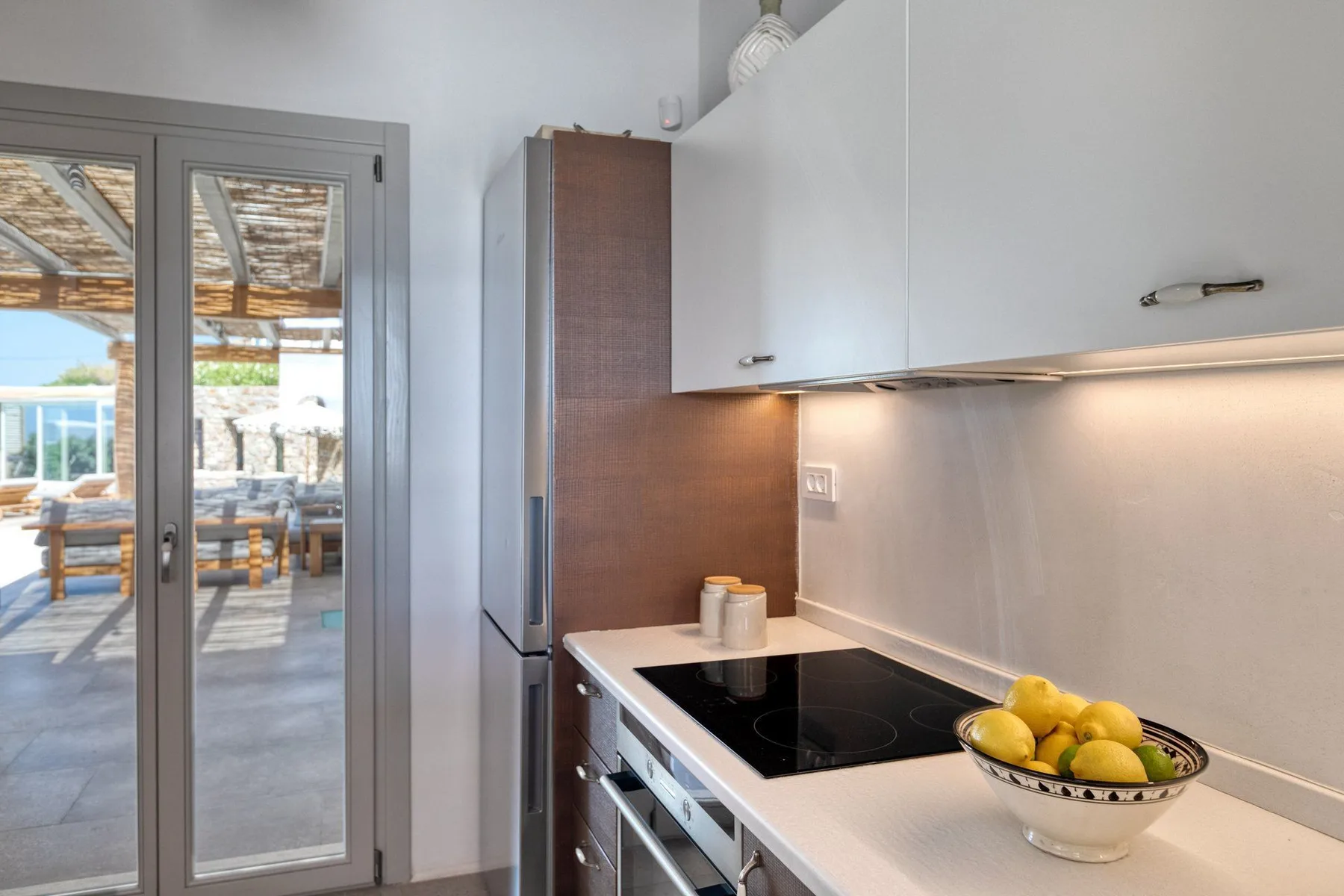 A modern kitchen with a cooktop and a glass door opening onto a patio.