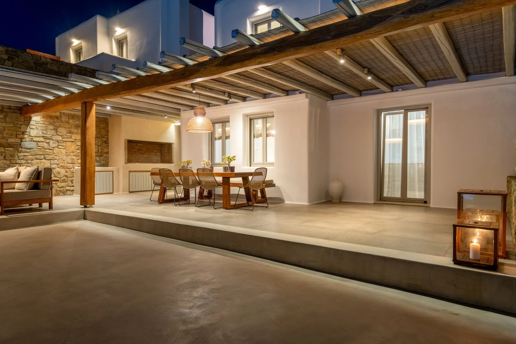 An outdoor dining area sits beneath a timber pergola beside a stone wall.