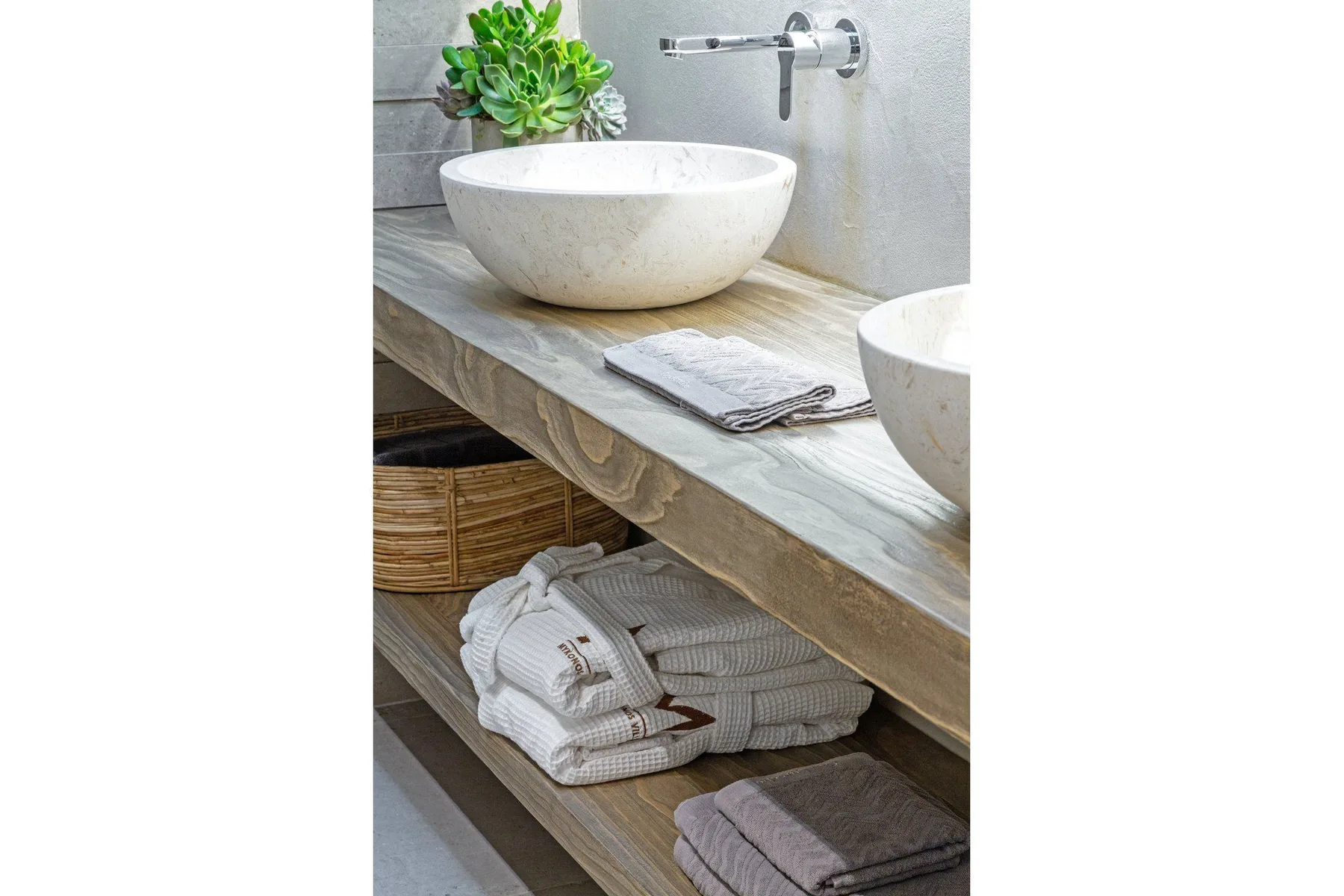 A bathroom vanity with vessel sinks, folded towels, and a small potted plant.