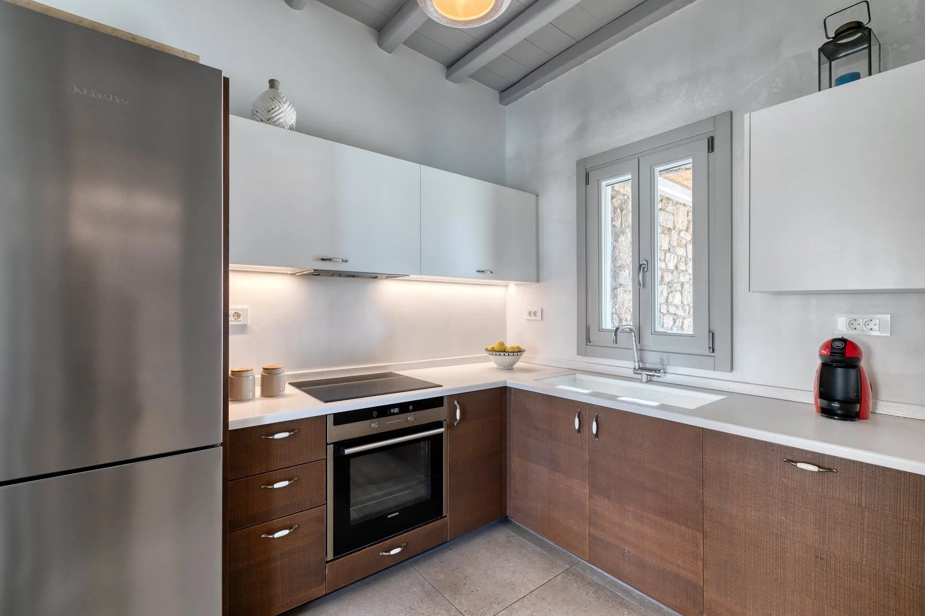 A modern kitchen with wood cabinetry, a cooktop, and a window above the sink.