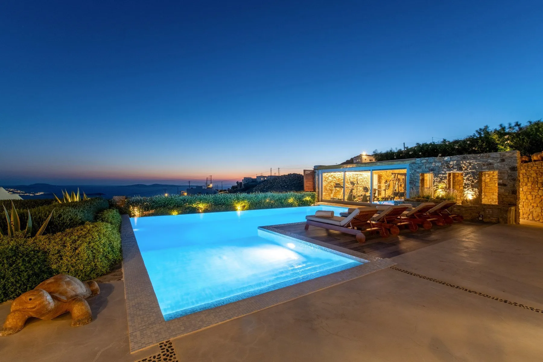 An illuminated outdoor swimming pool beside a warmly lit building at dusk.