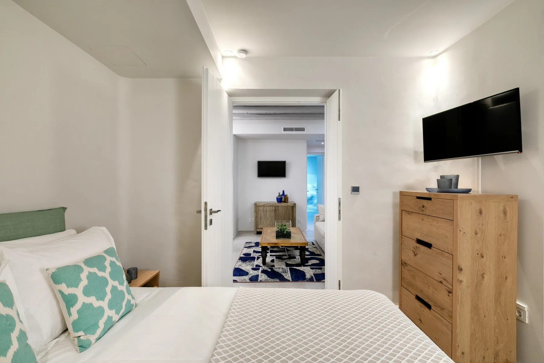 A bedroom with a bed, a wooden dresser, and a wall-mounted television.