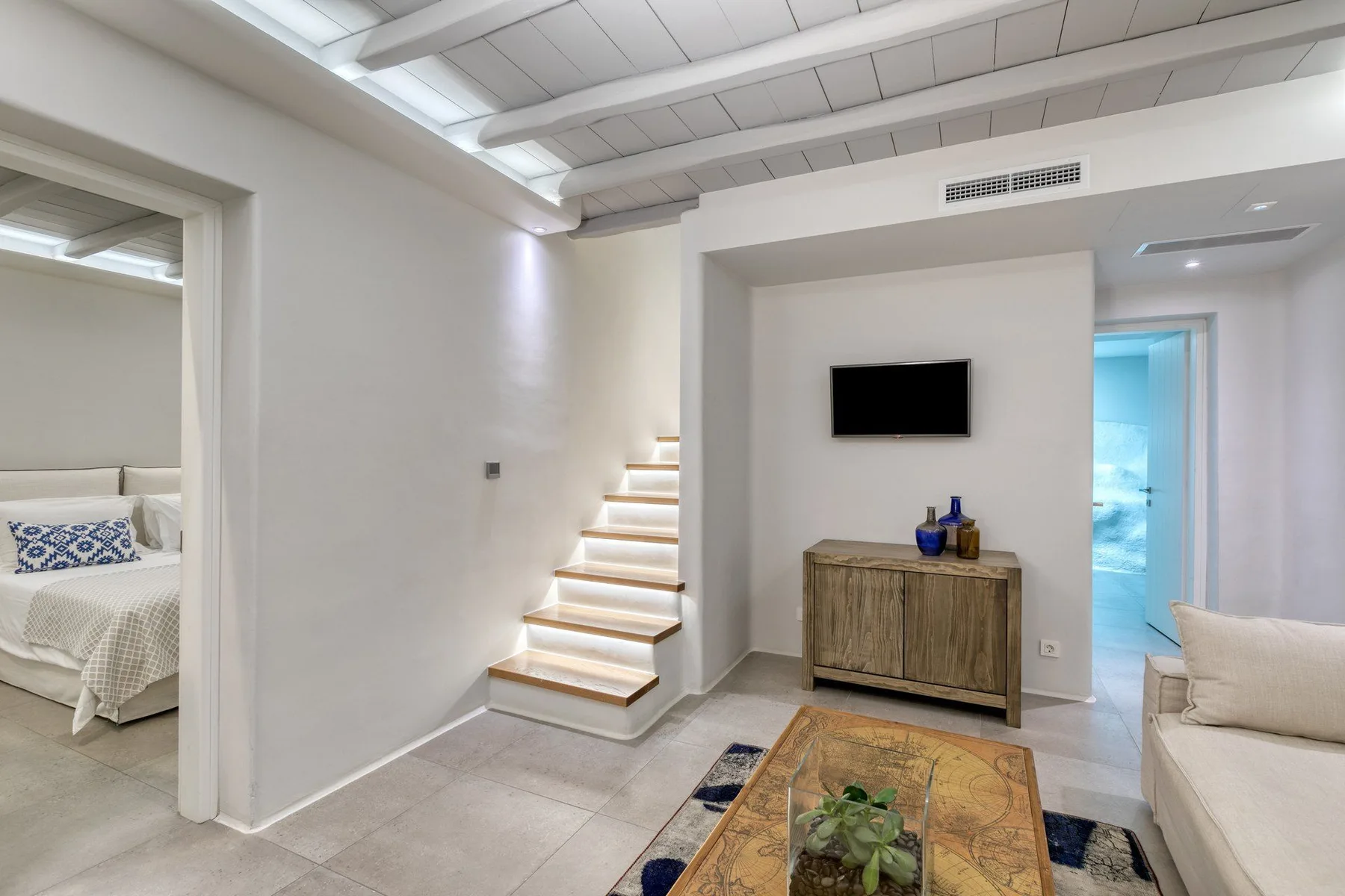 A bright living area with a staircase and a television above a cabinet.