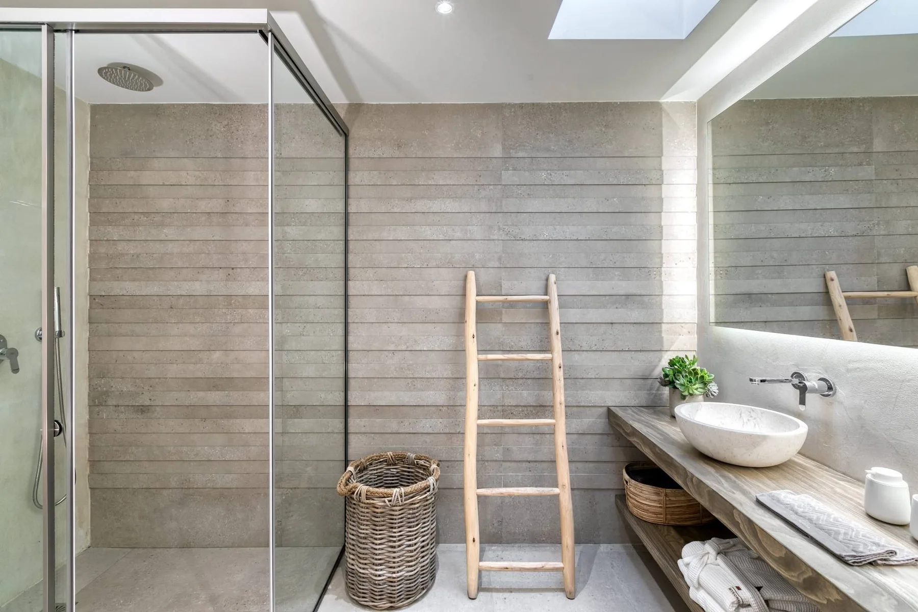 A bright bathroom with a glass shower, a wooden ladder, and a sink.