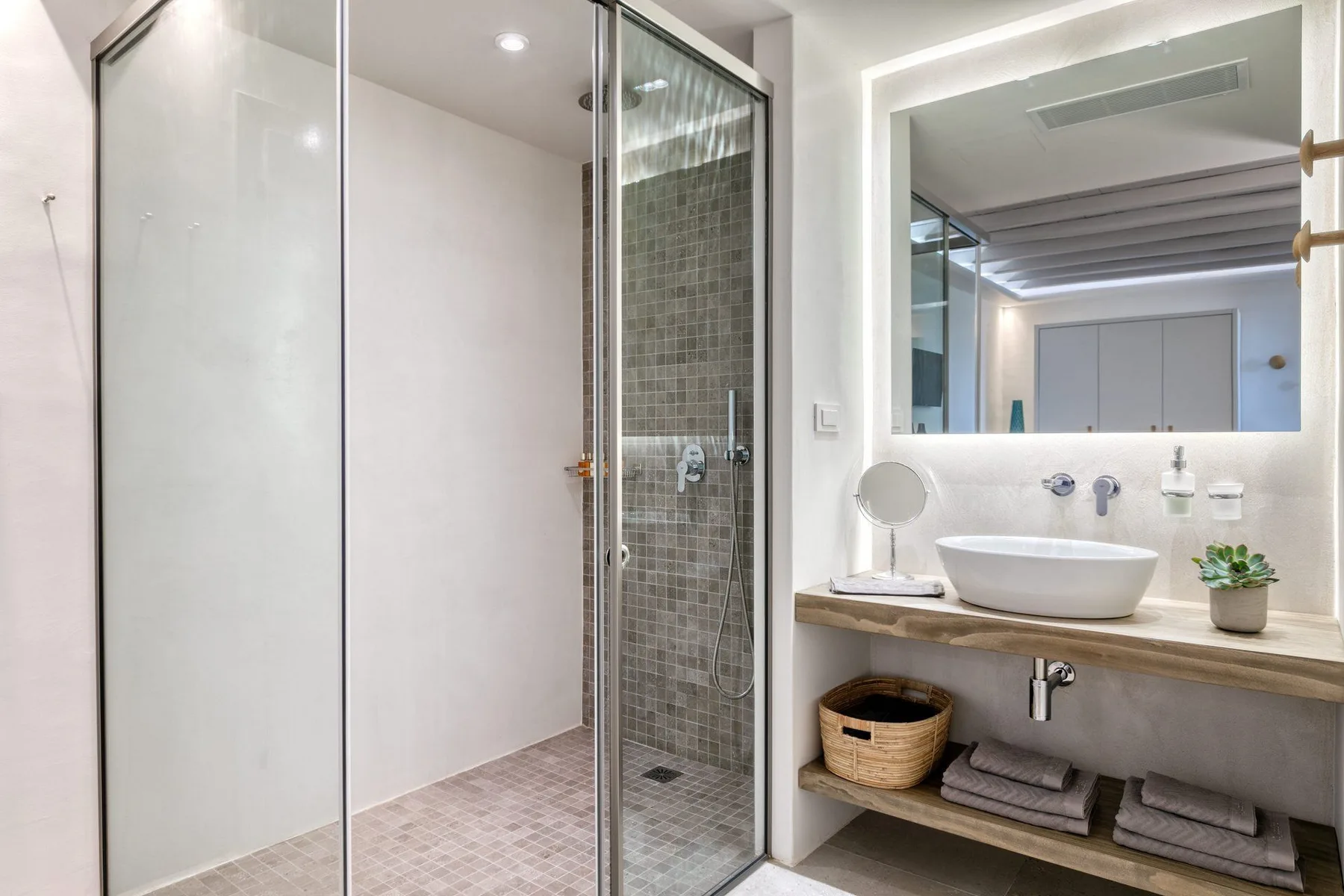 A bright bathroom with a glass shower and a vanity beside a large mirror.