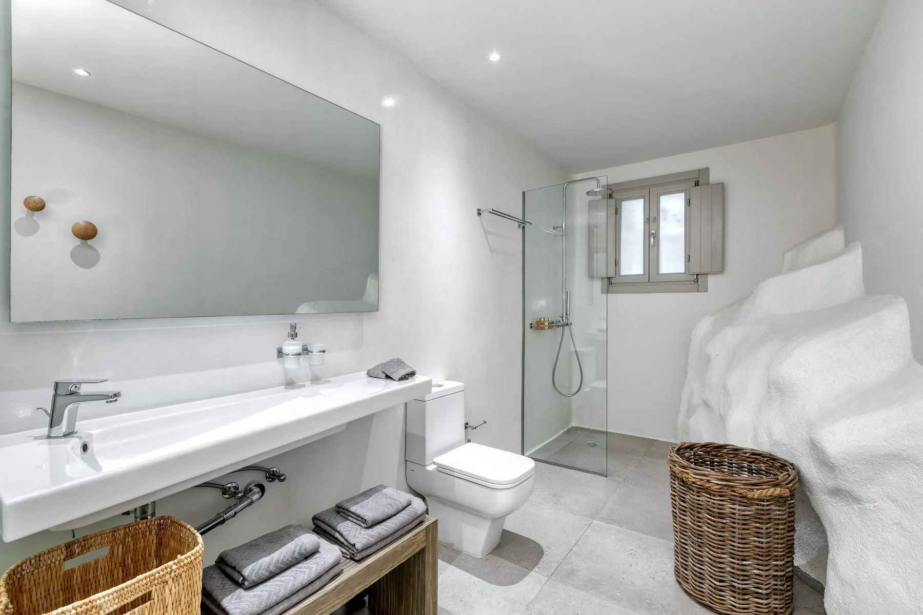 A bright bathroom with a long sink counter, shower, and window.