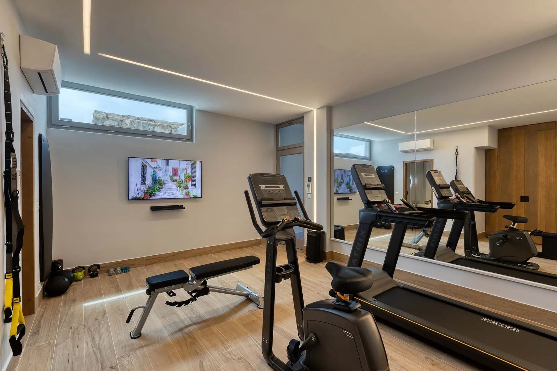 Un gimnasio con cintas de correr, una bicicleta estática y una pantalla en la pared.