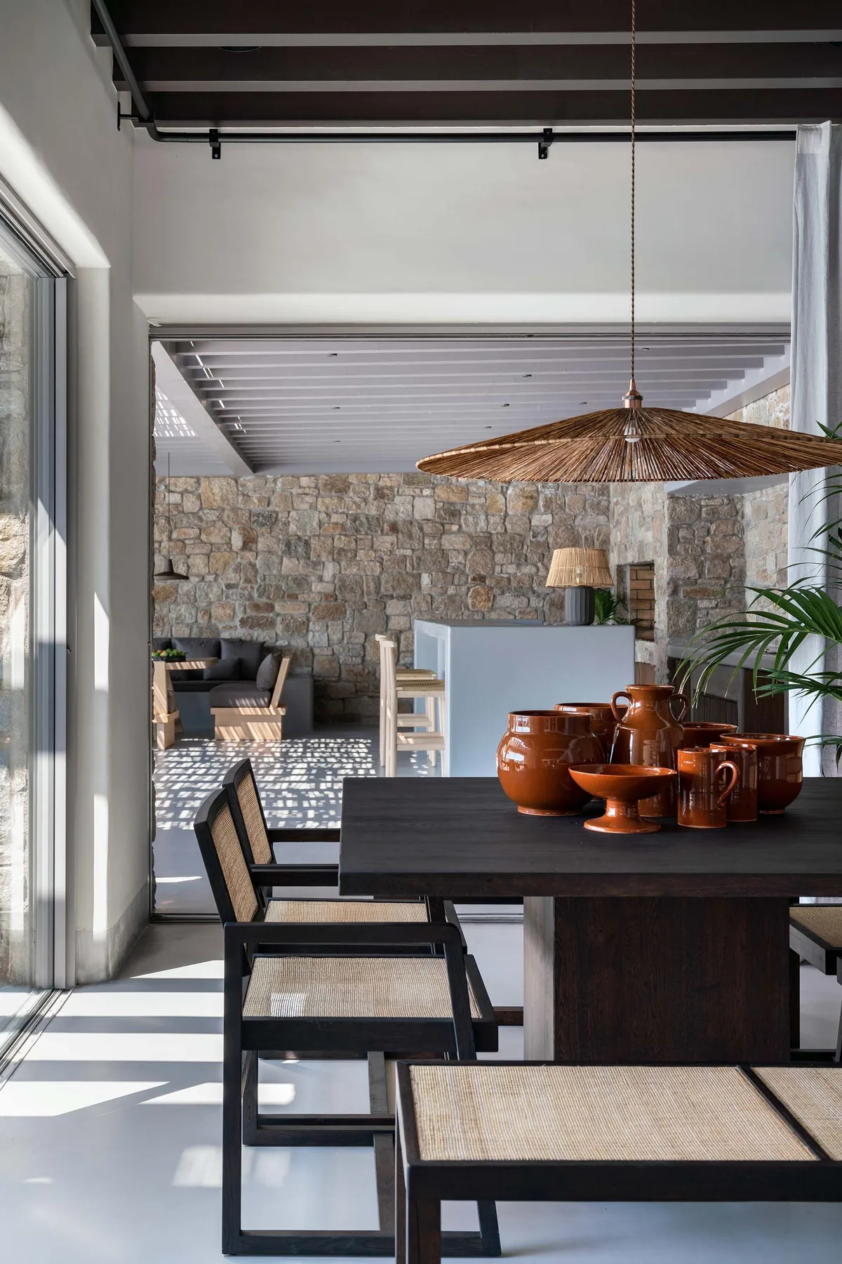 Un comedor con una mesa oscura y una lámpara colgante tejida junto a una pared de piedra.
