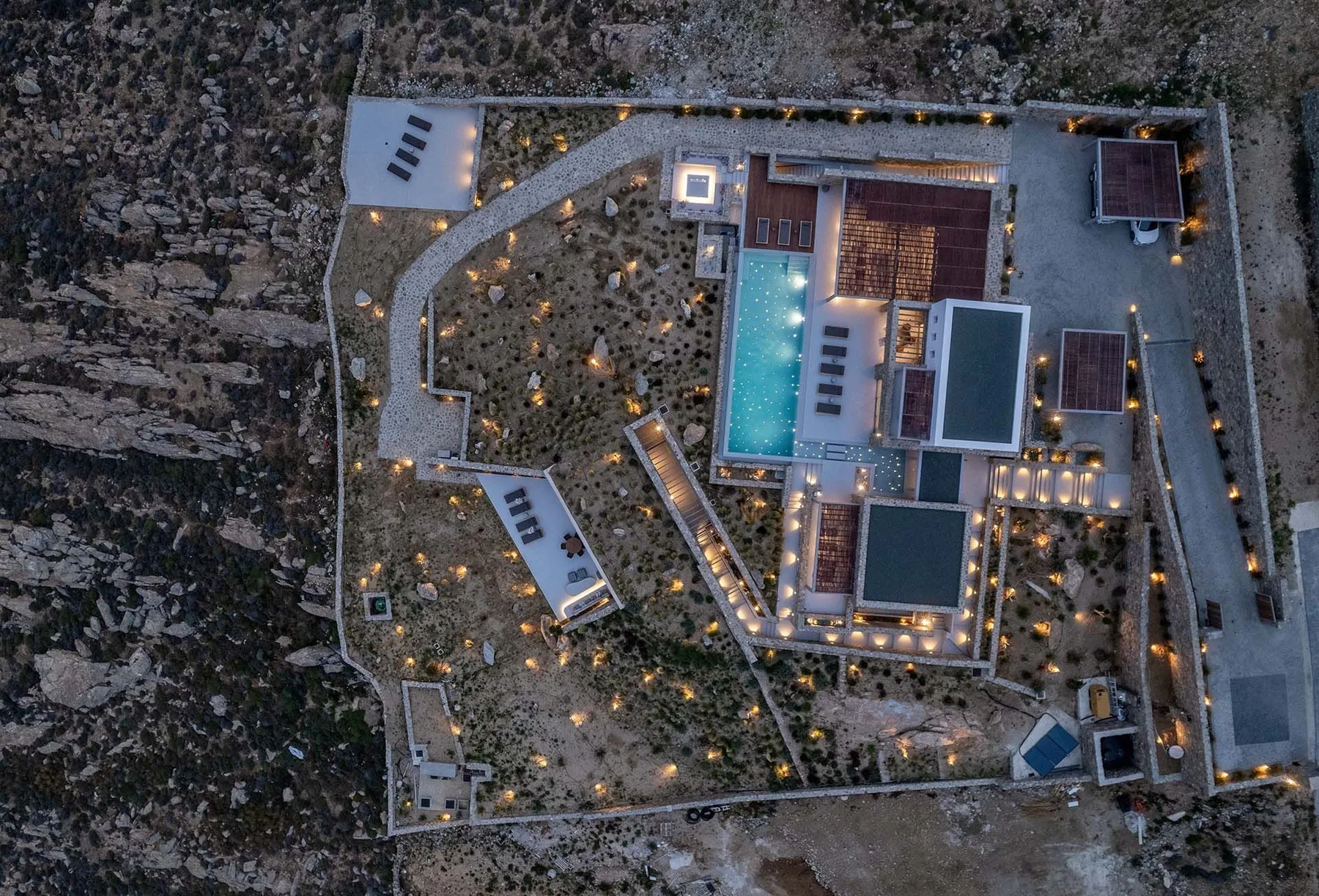 Vista aérea de una propiedad moderna con piscina iluminada y jardines.
