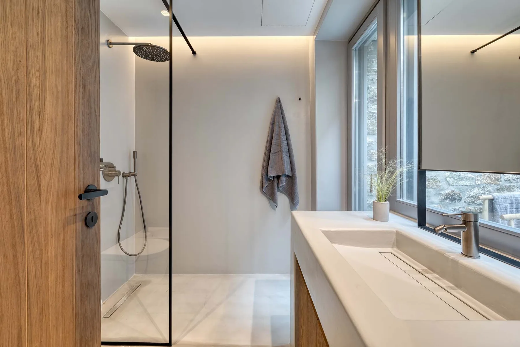 Un baño moderno con ducha y un largo tocador junto a una ventana amplia.