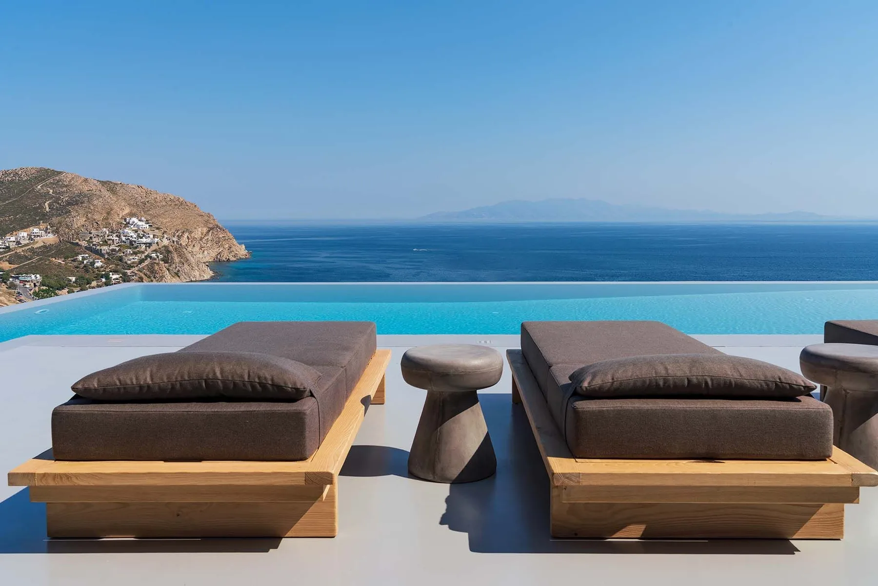 Una zona de asientos junto a la piscina al aire libre mira al mar y a una costa rocosa.
