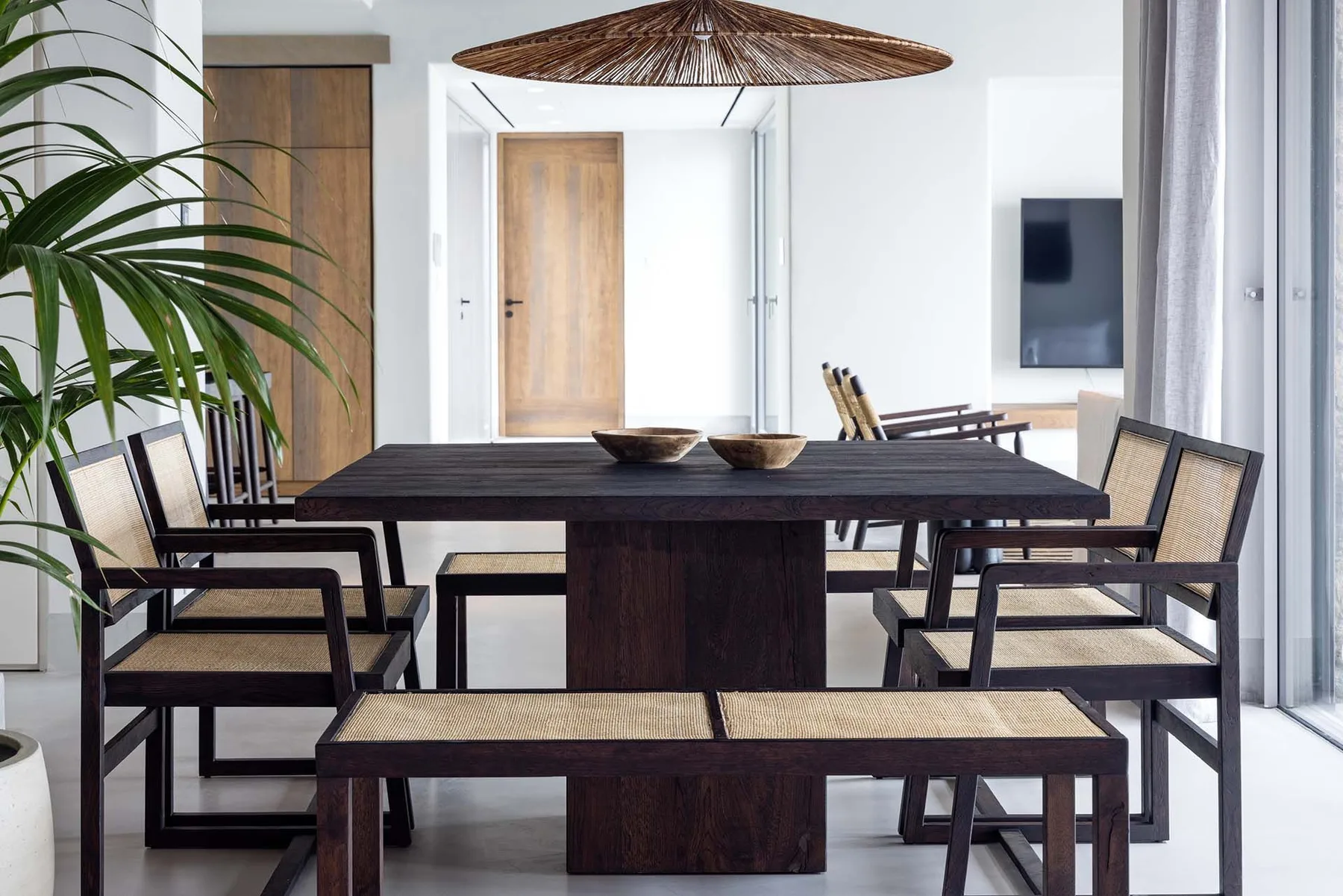 Un comedor con una mesa oscura, sillas y una lámpara colgante tejida.