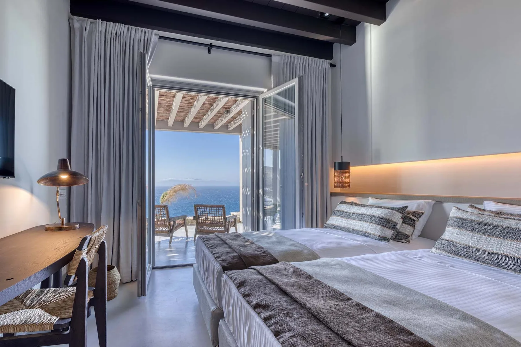 Un dormitorio con camas junto a puertas abiertas con vistas al mar.