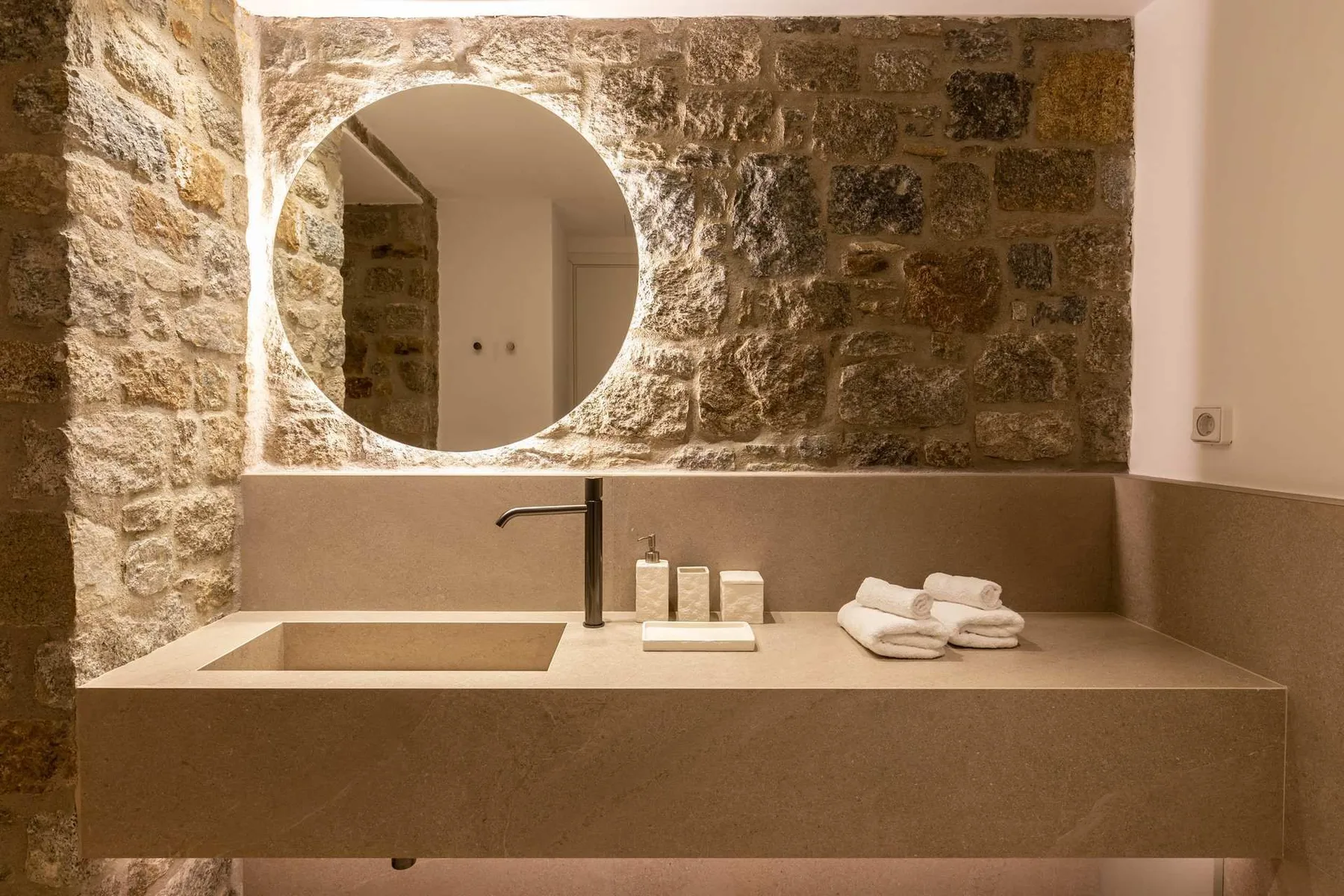 A bathroom vanity with a round mirror and folded towels.