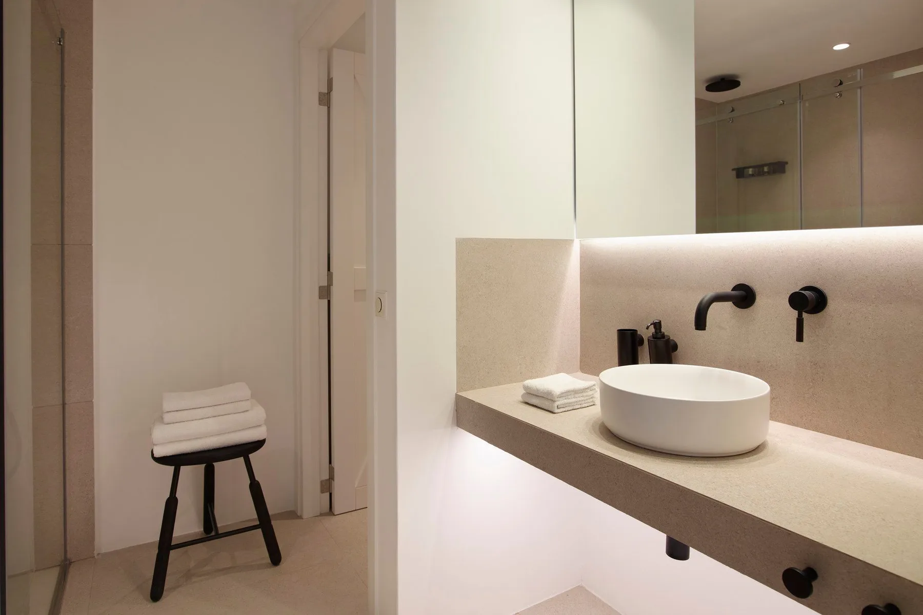 A bright bathroom vanity with a vessel sink and a shower visible behind it.