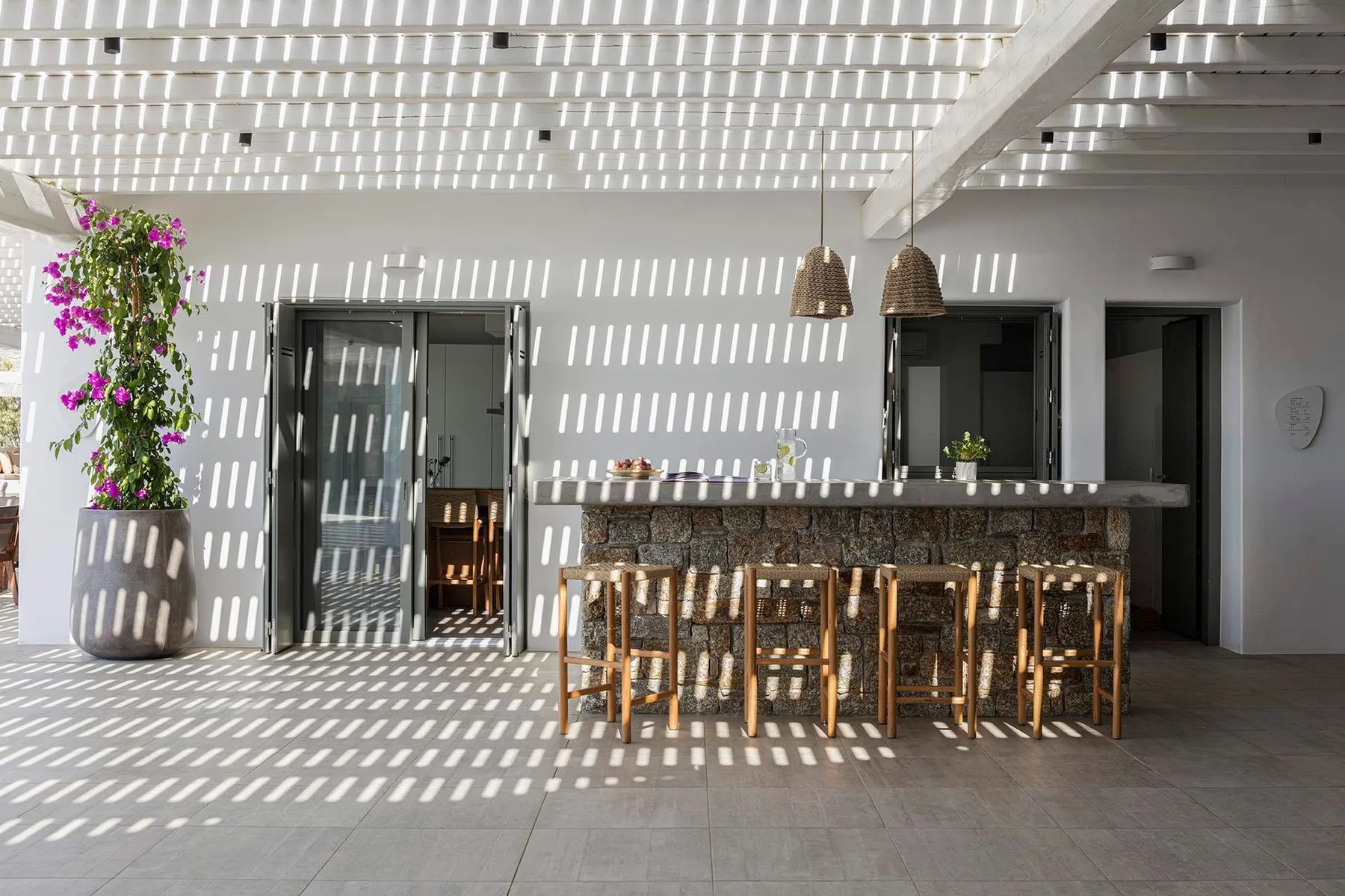 Outdoor dining area with a long counter, wooden seating, and a slatted pergola overhead.