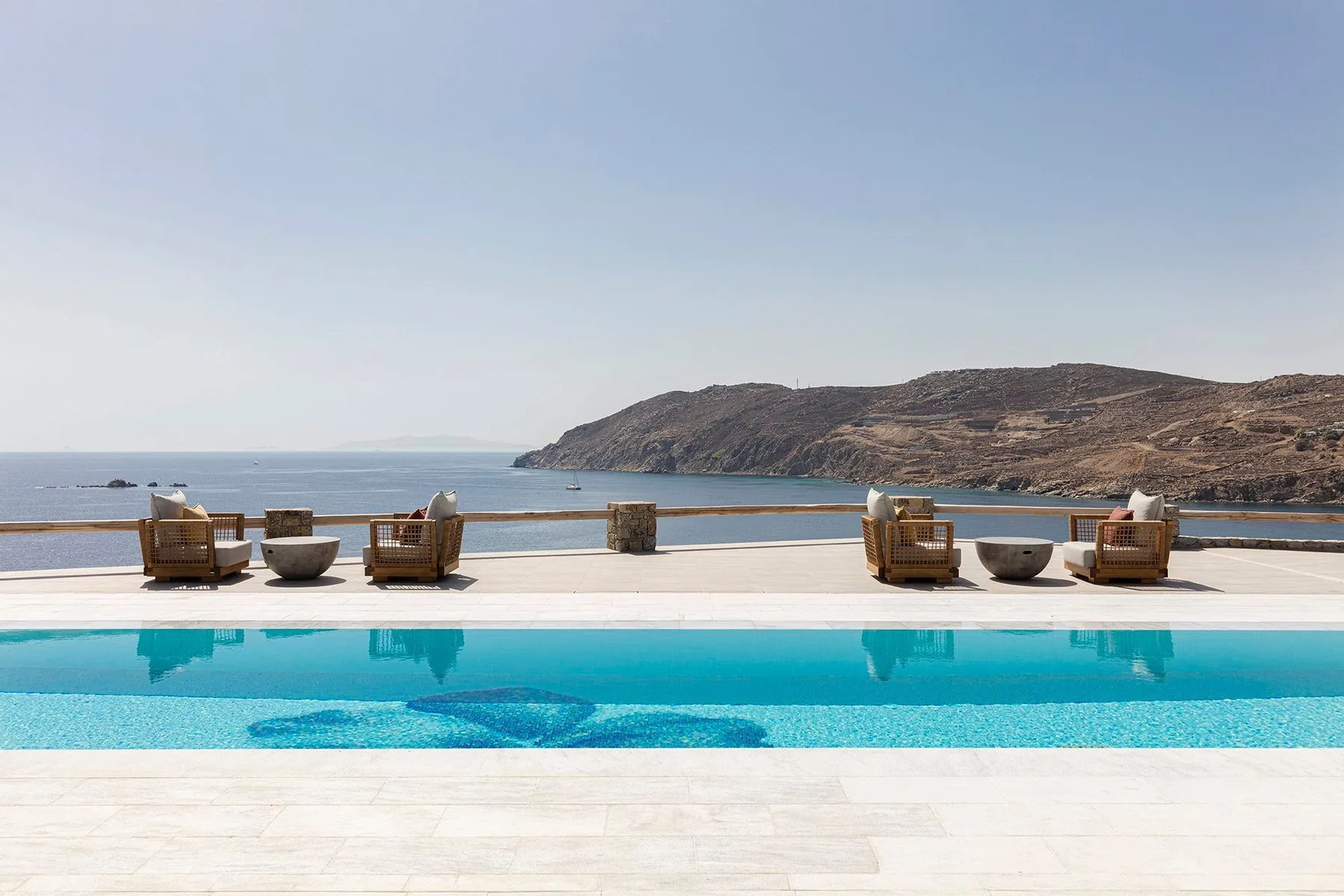 An outdoor swimming pool overlooks the sea, with seating arranged along the deck.