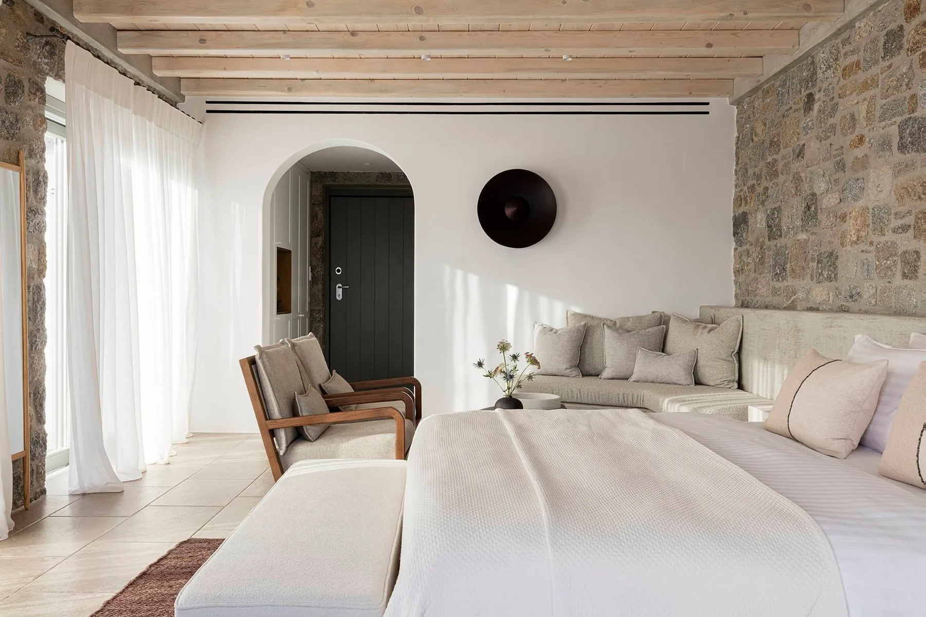 A bright bedroom with a large bed, seating, and stone walls.