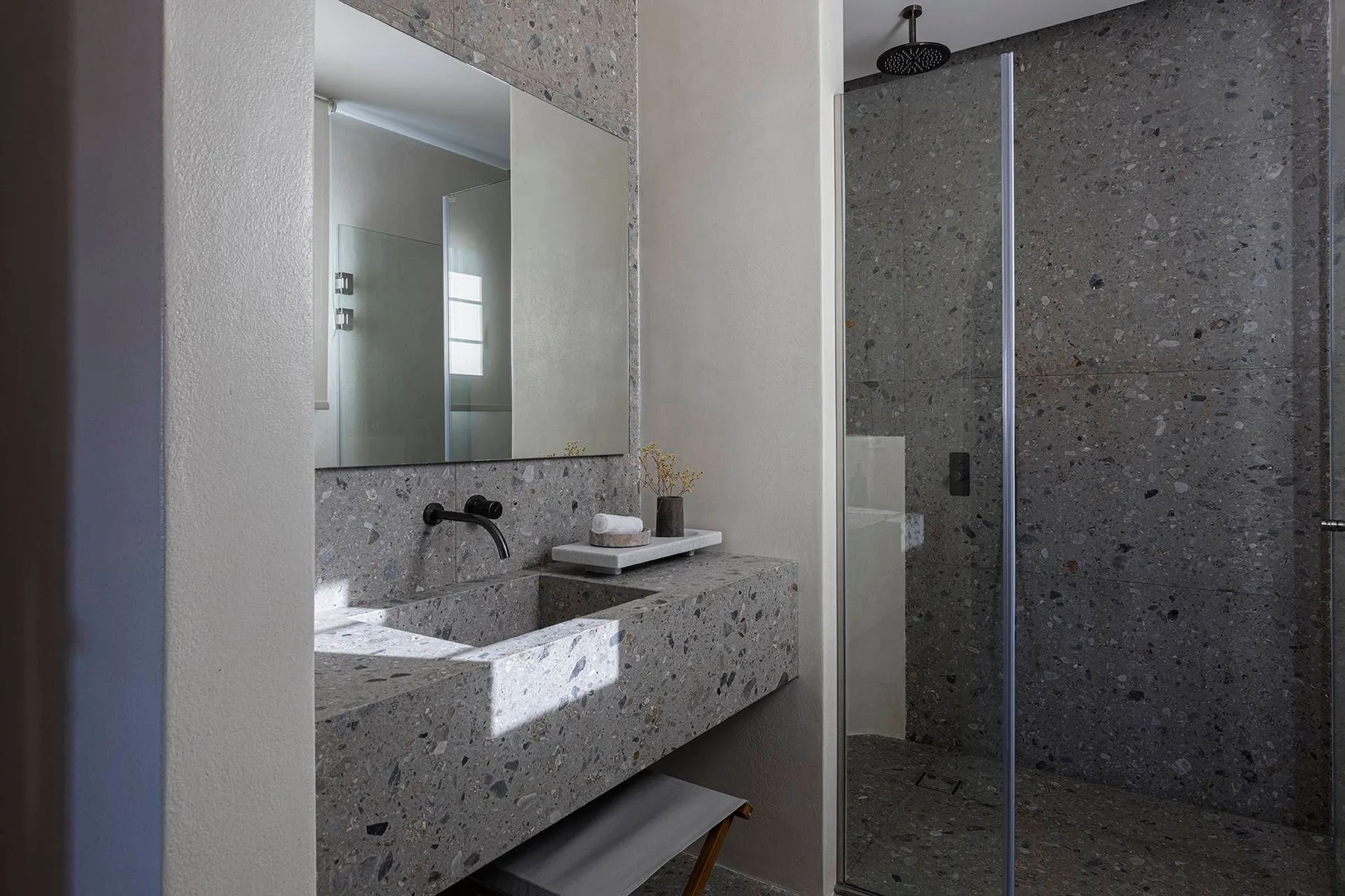 A modern bathroom with a stone vanity and glass shower.