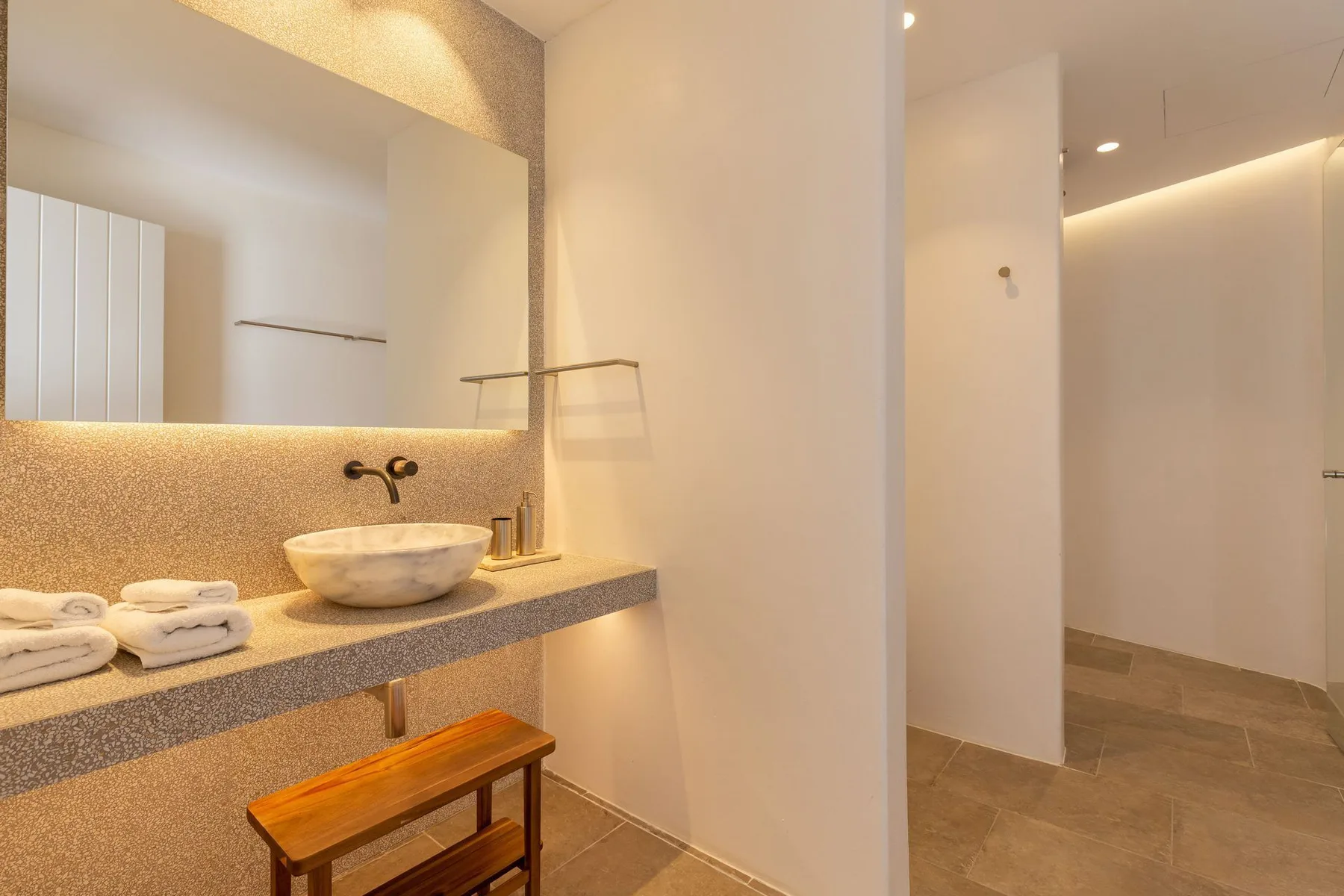 A bright bathroom with a vessel sink, wall mirror, and open shower area.