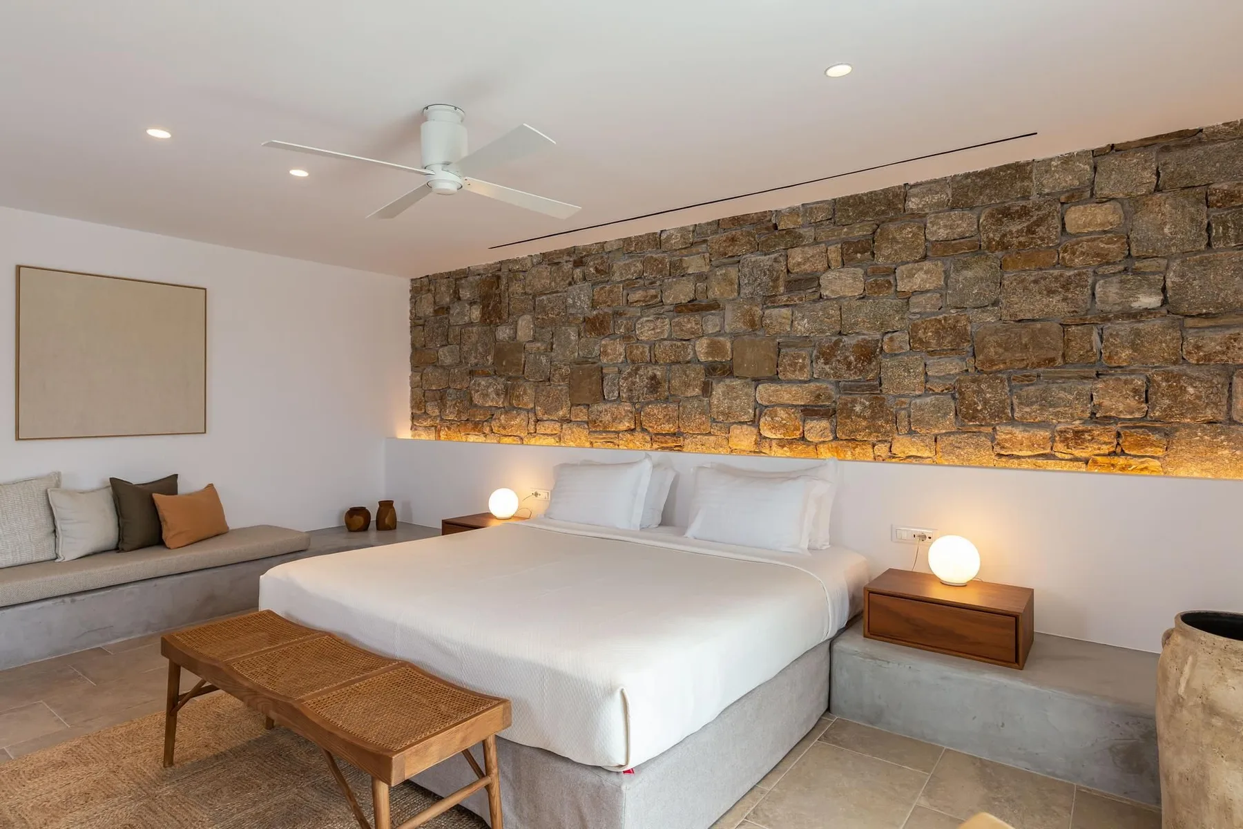 A bedroom with a large bed, a stone accent wall, and a seating area.