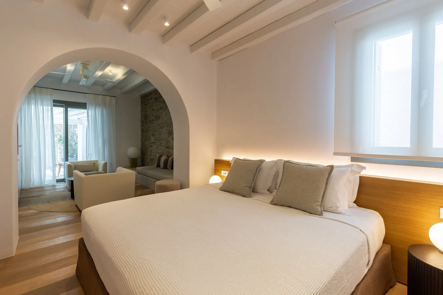 A bedroom with a large bed and an arched opening to a sitting area.
