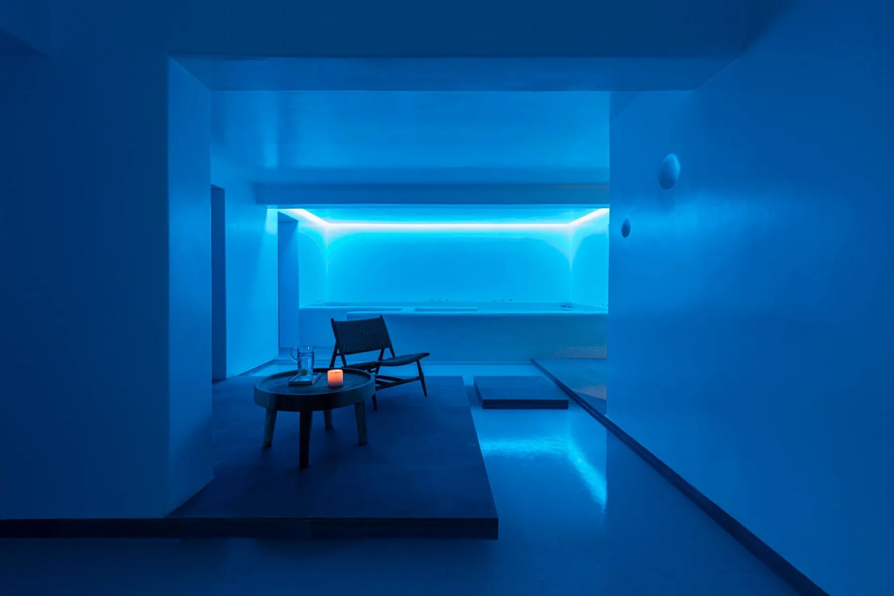 A blue-lit indoor pool area with a small seating arrangement beside the water.