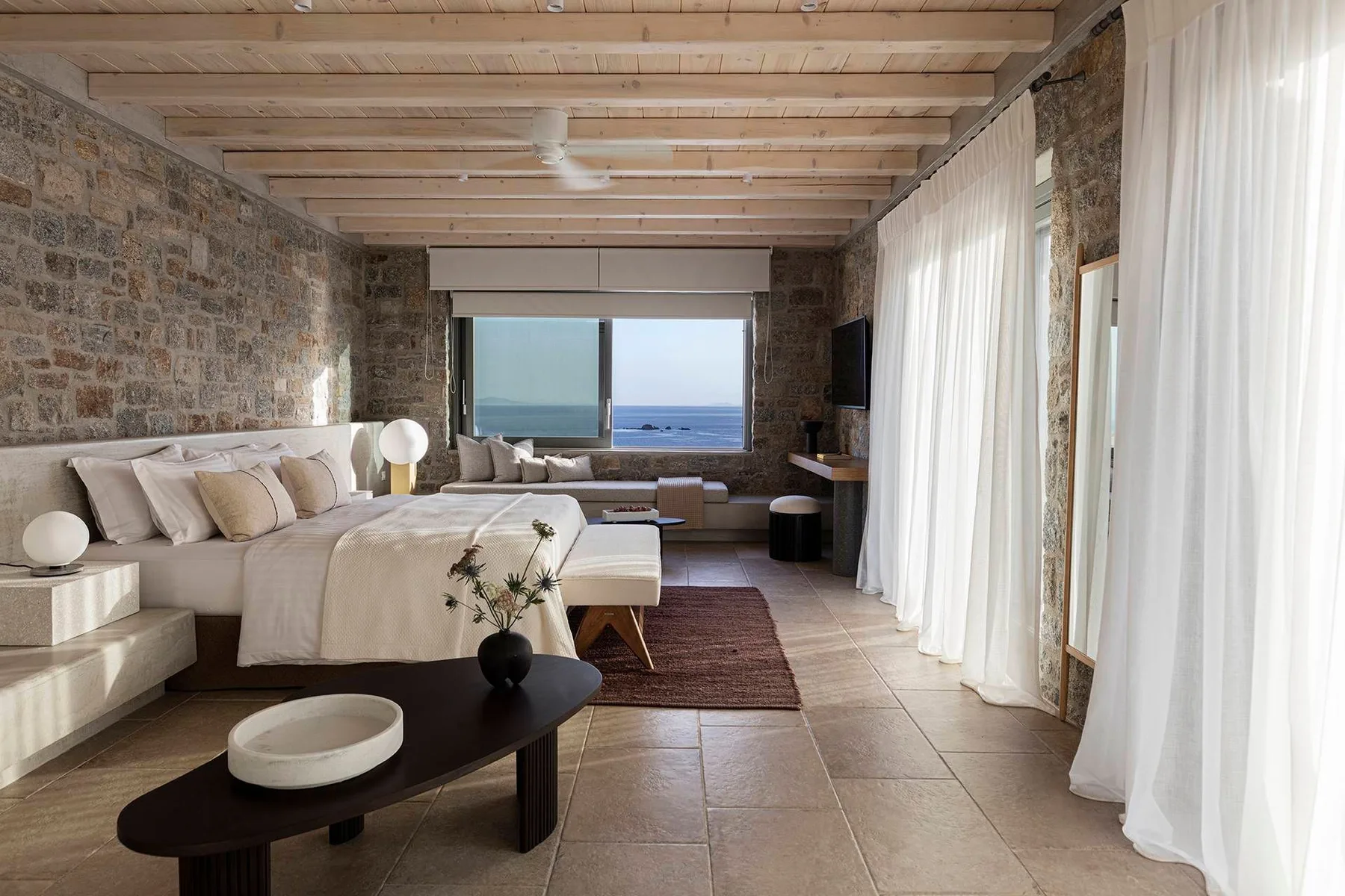 A stone-walled bedroom with a bed and a window overlooking the sea.