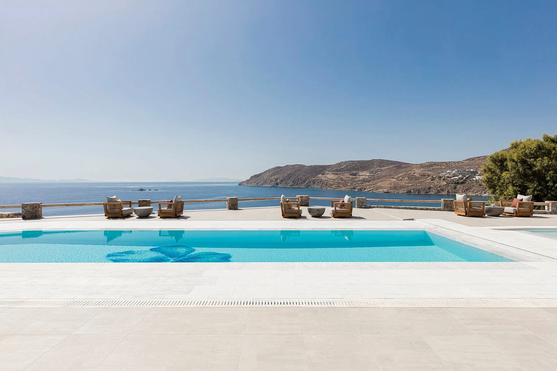 An outdoor swimming pool overlooks the sea, with lounge seating along the far edge.