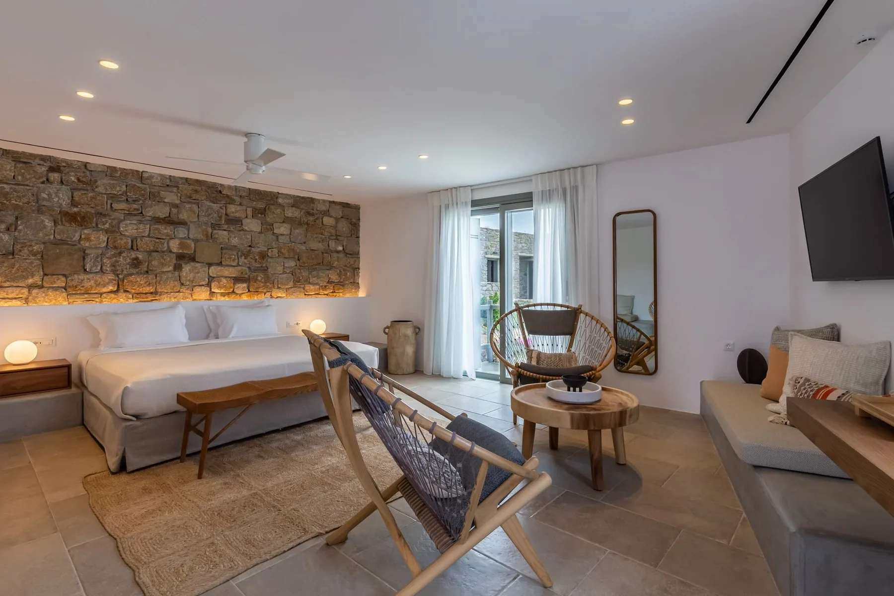 A modern living room with a bed, seating, and a stone accent wall.