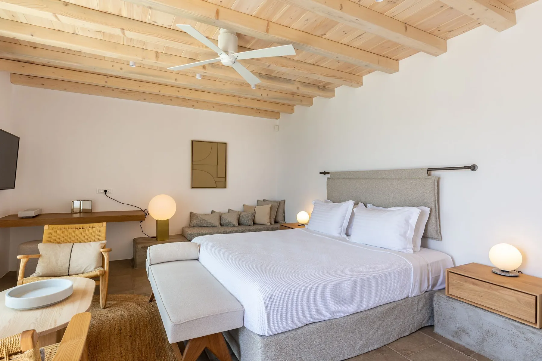 A bedroom with a large bed, a desk, and exposed wooden ceiling beams.
