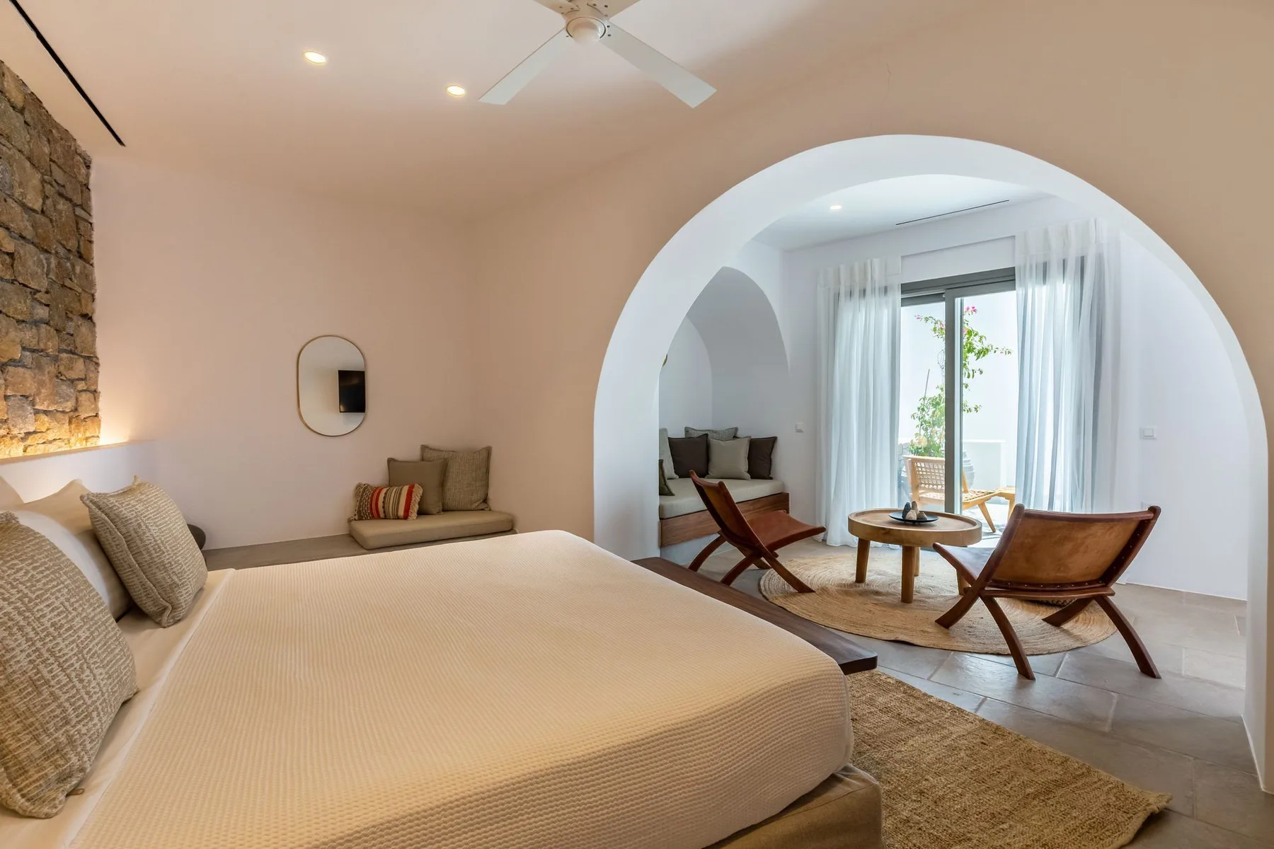 A bedroom with a large bed opens through an arch to a bright sitting area.