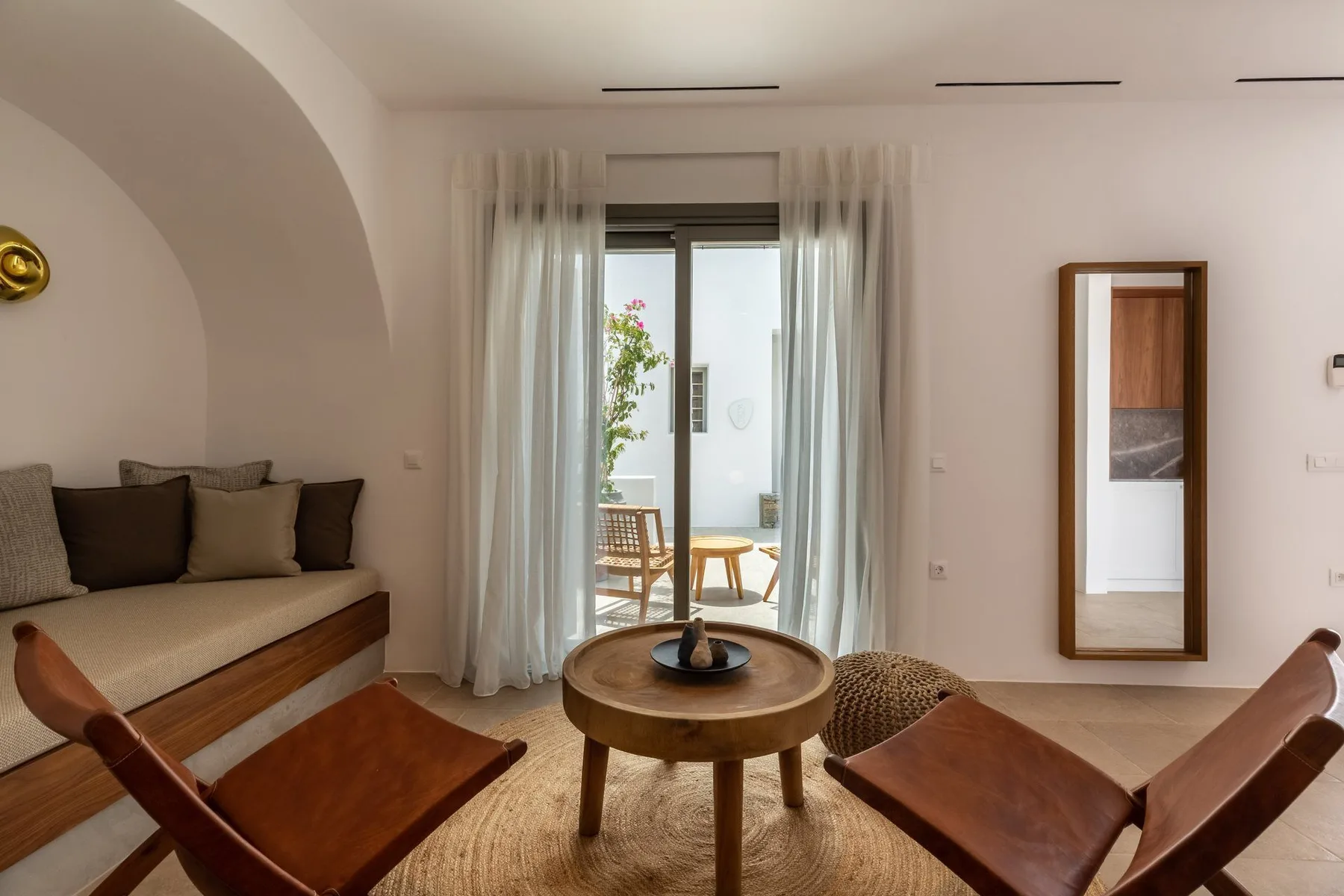 A bright living room with seating around a round wooden coffee table and glass doors.