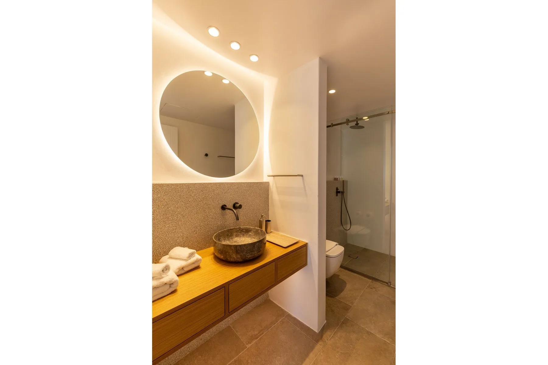 A bathroom with a round mirror, a sink, and a glass shower.