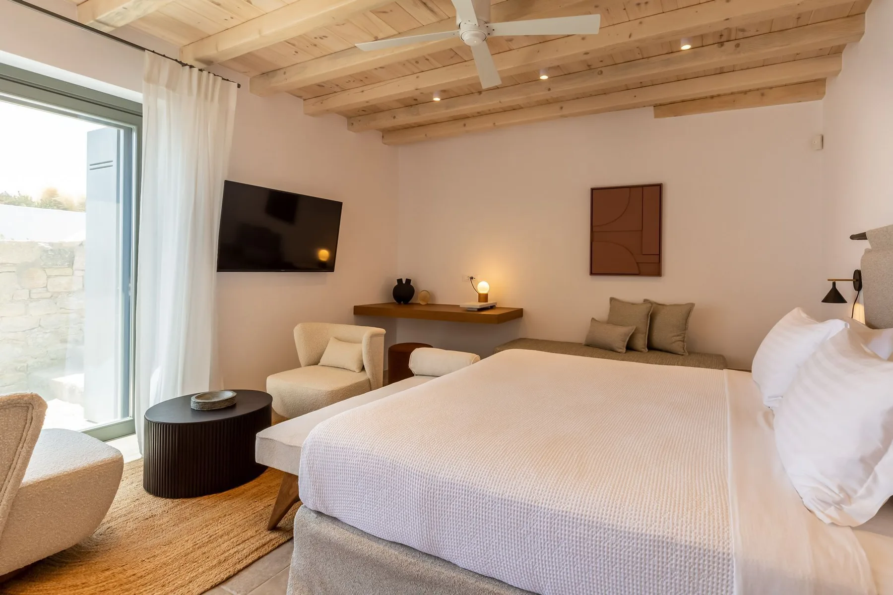 A bedroom with a large bed, seating area, and exposed wooden ceiling beams.