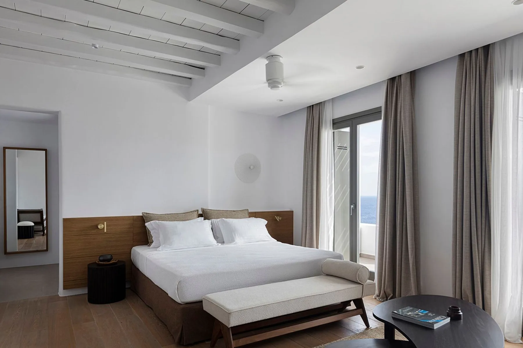 A bright bedroom with a neatly made bed beside tall curtained windows.