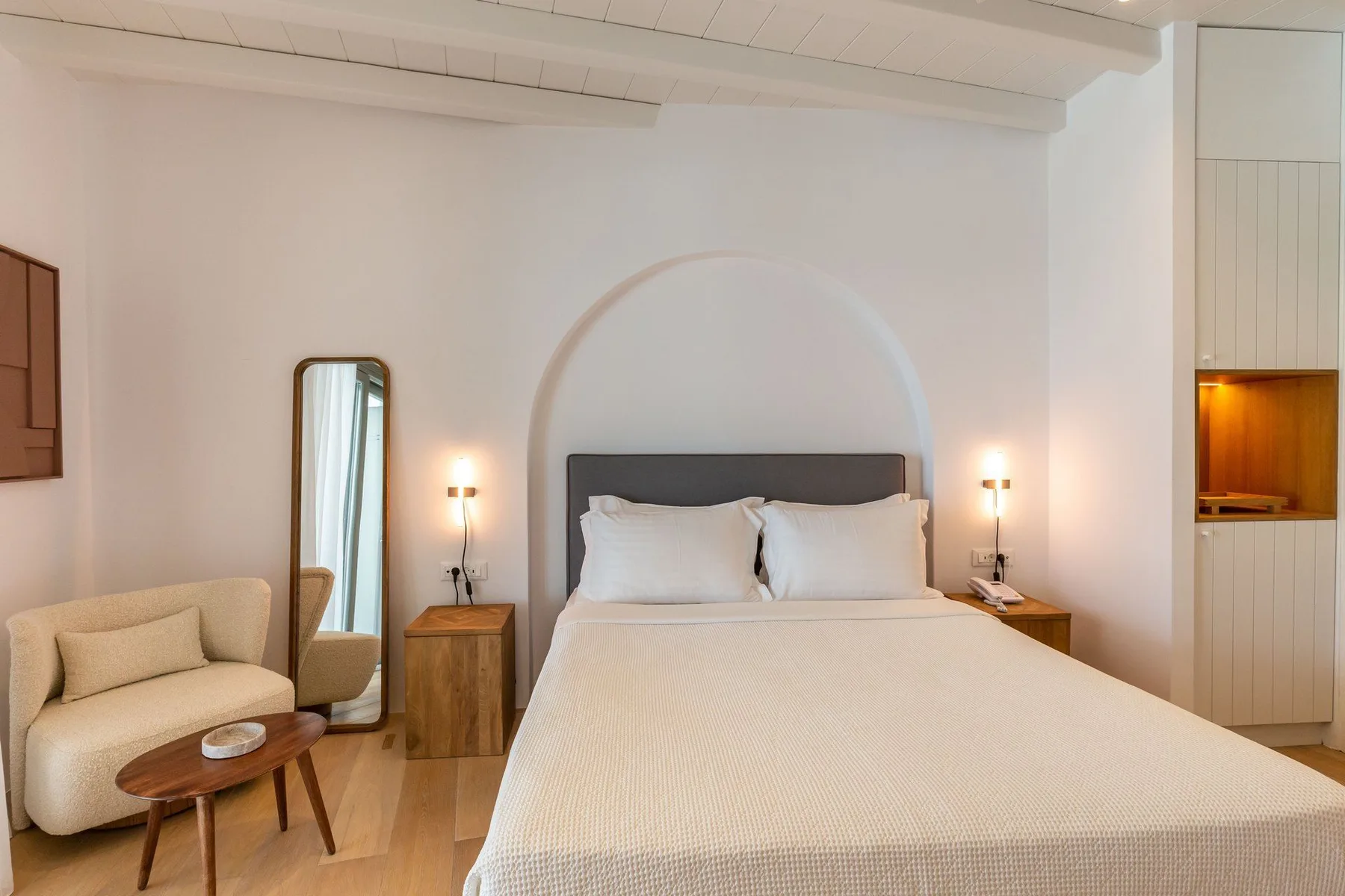 A bedroom with a neatly made bed, bedside tables, and a full-length mirror.