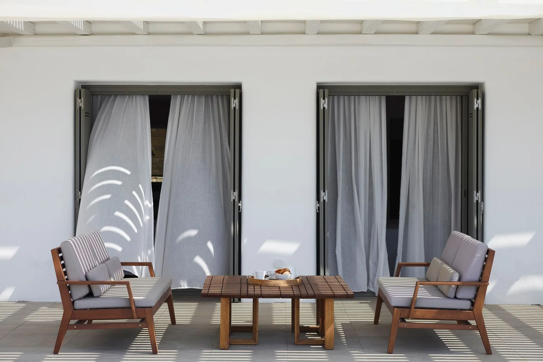 An outdoor seating area with two chairs and a low table in front of curtained doors.