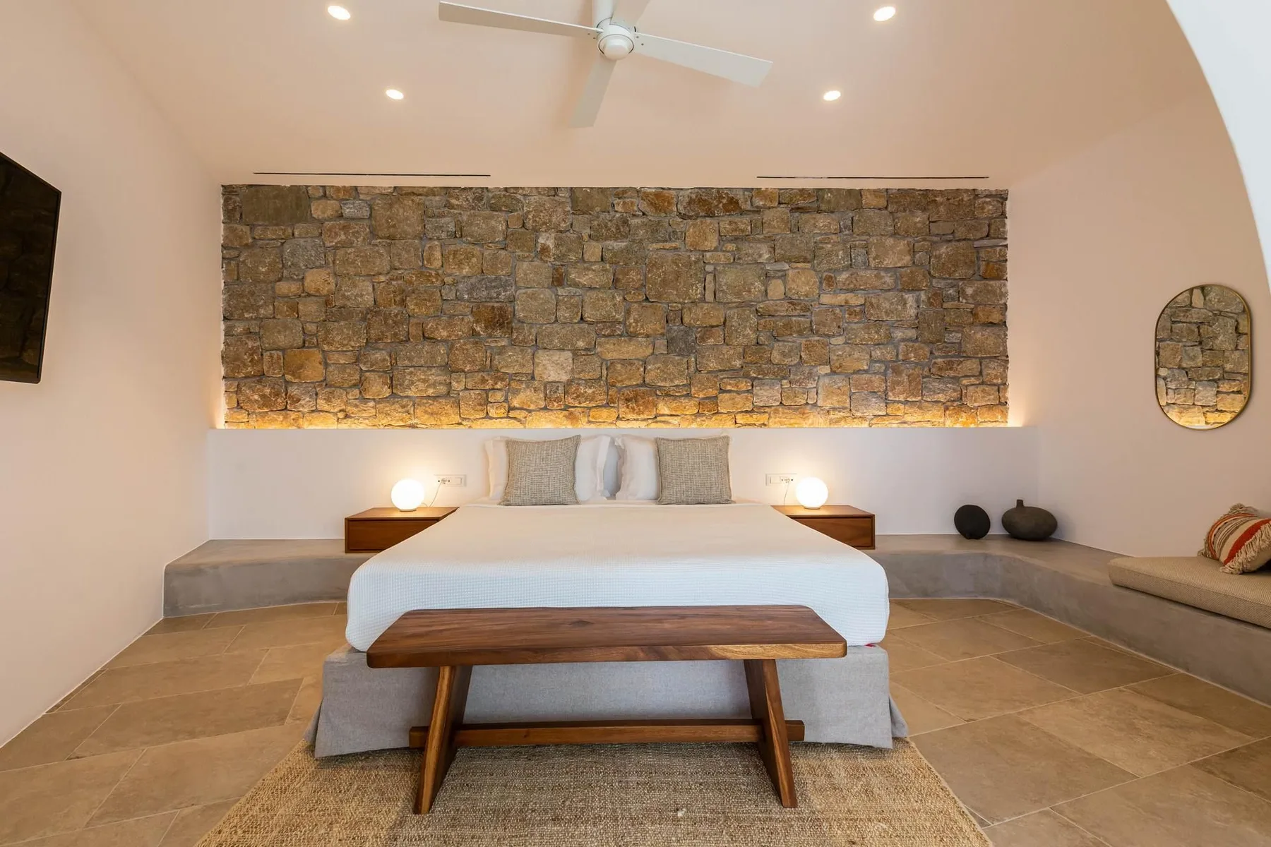A bedroom with a bed beneath a stone accent wall and built-in seating.