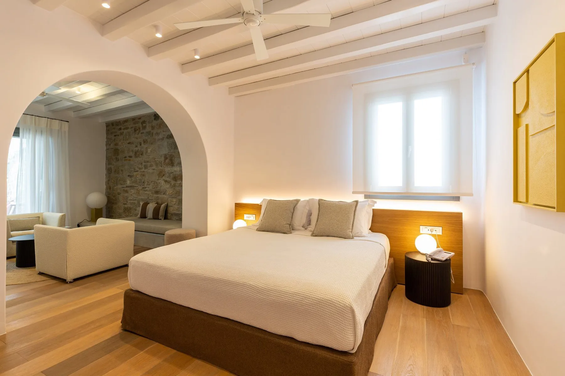 A bright bedroom with a large bed and a seating area beyond an archway.