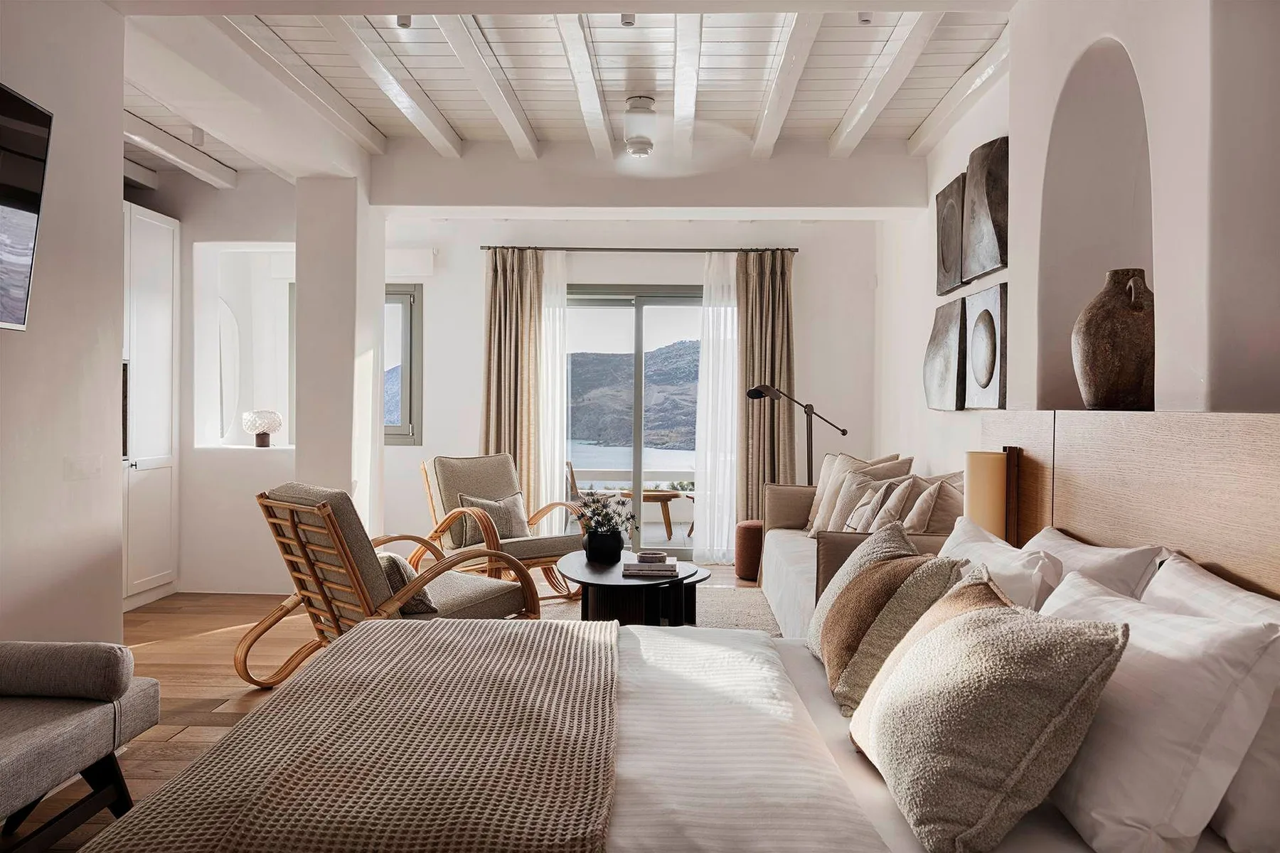 A bright living room with seating, a coffee table, and a large window overlooking the water.
