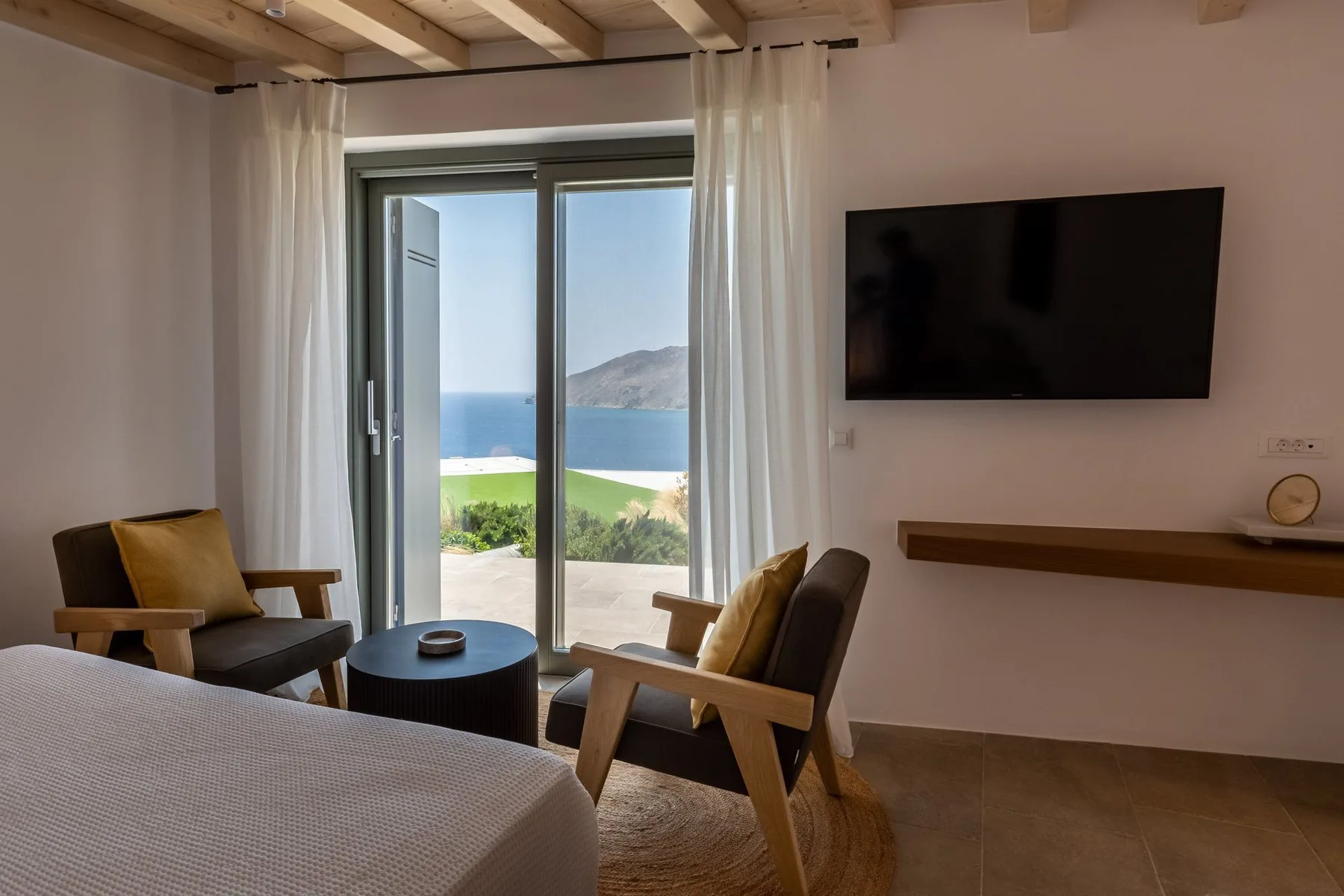 A bedroom sitting area with a bed, armchairs, and a view through the glass doors.
