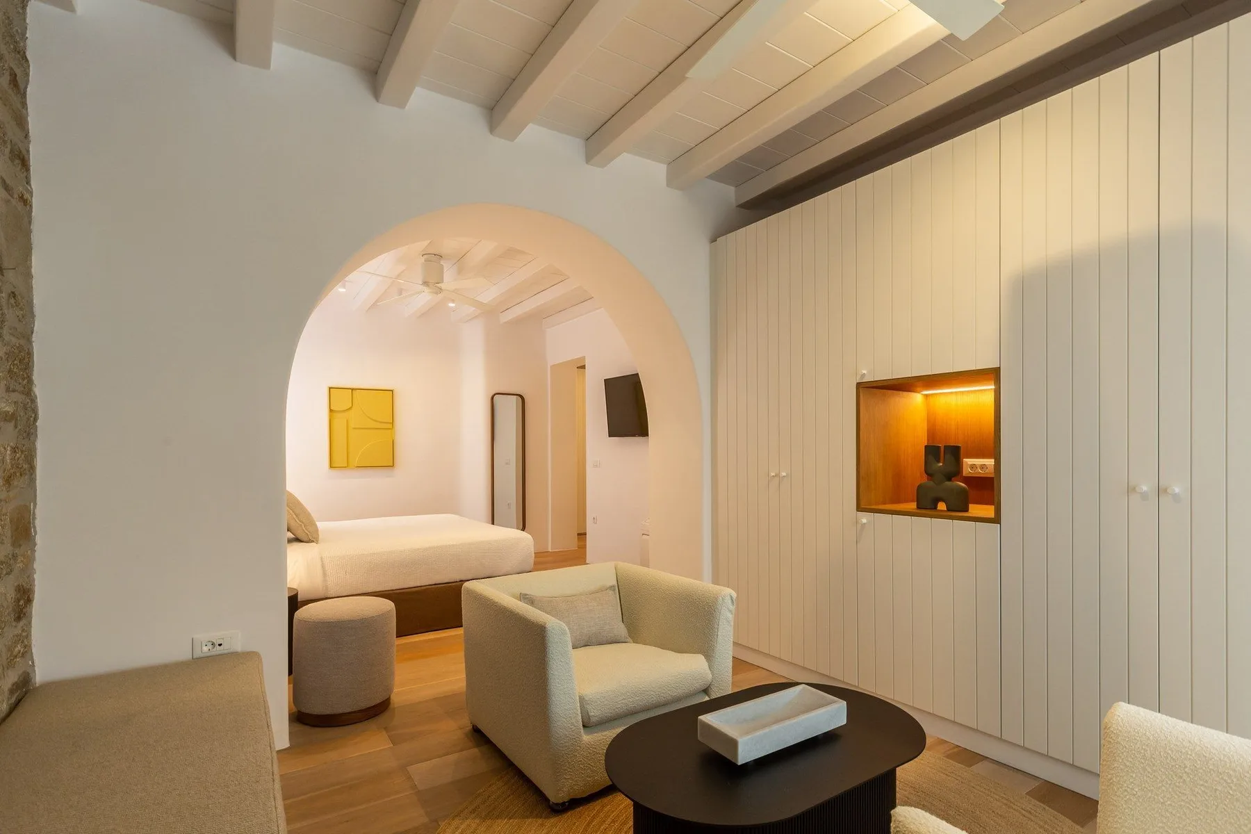 A living area with seating sits beside a bedroom visible through an arched opening.