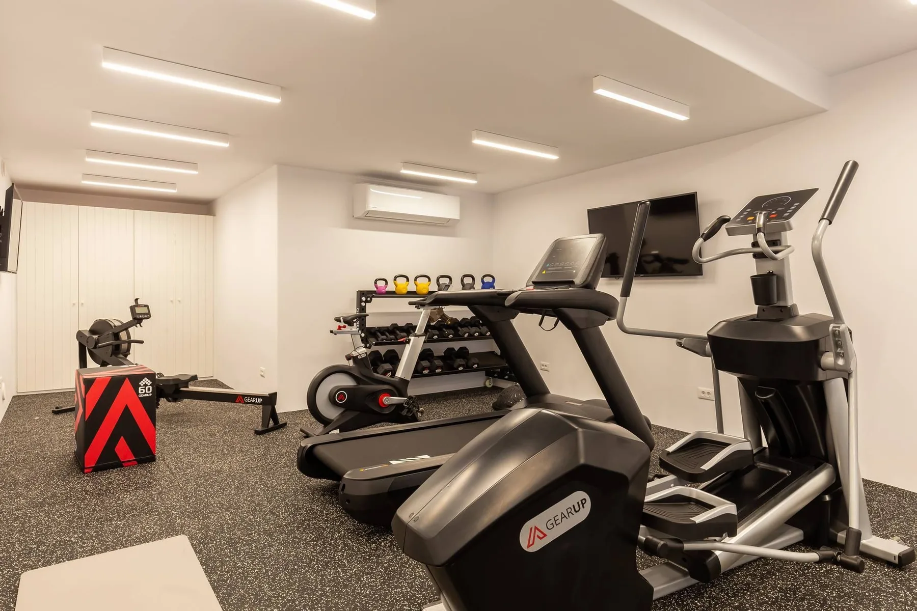 A gym with exercise machines, treadmills, and a rack of weights.