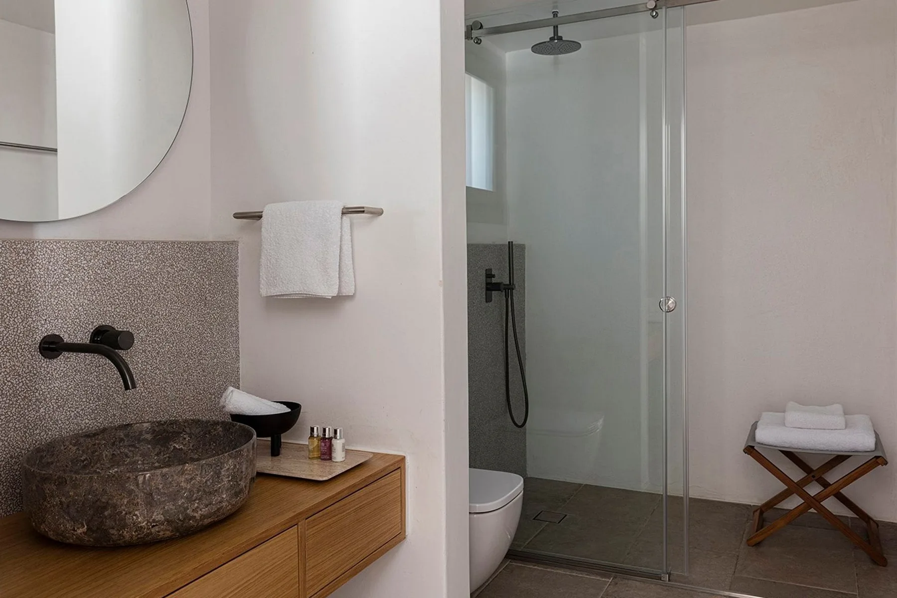 A modern bathroom with a stone basin beside a glass shower.