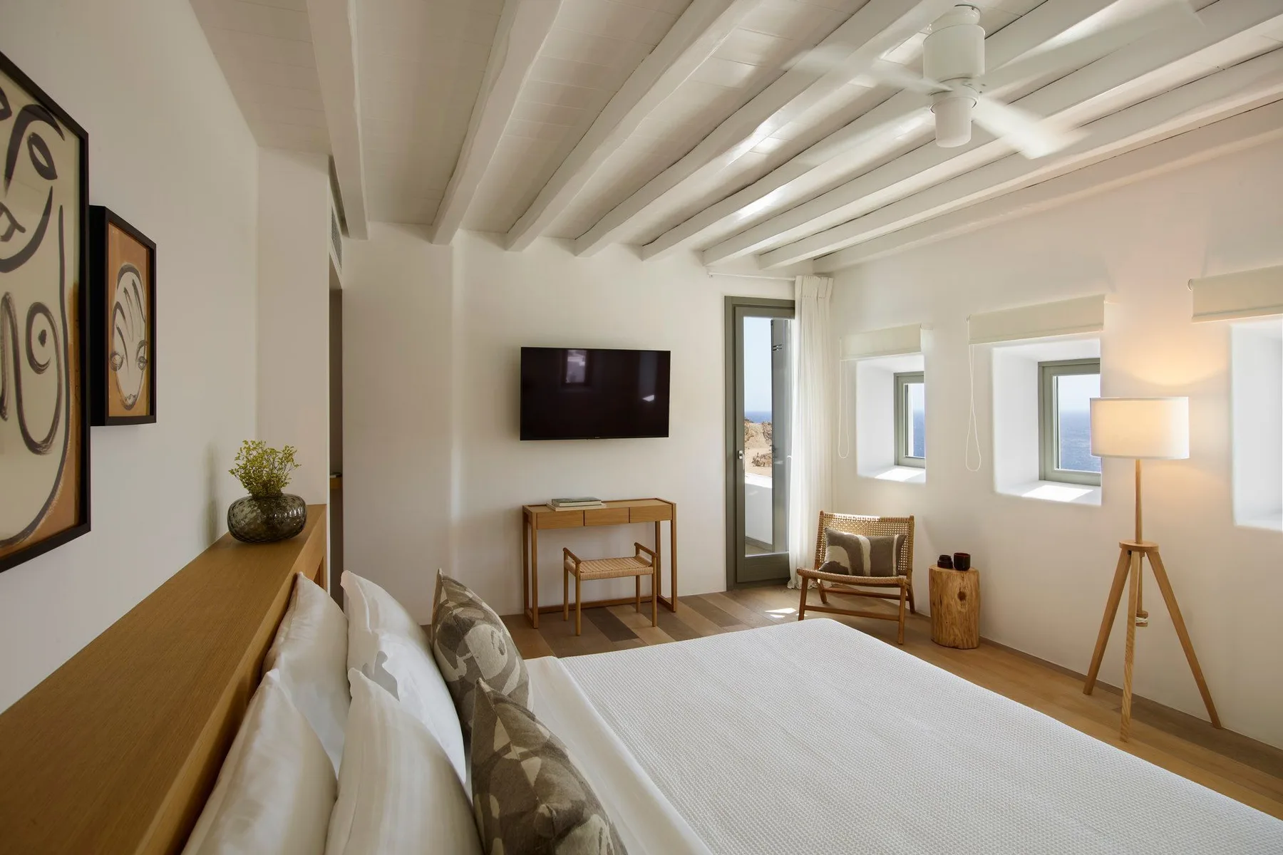 A bright bedroom with a large bed, wall-mounted television, and windows.